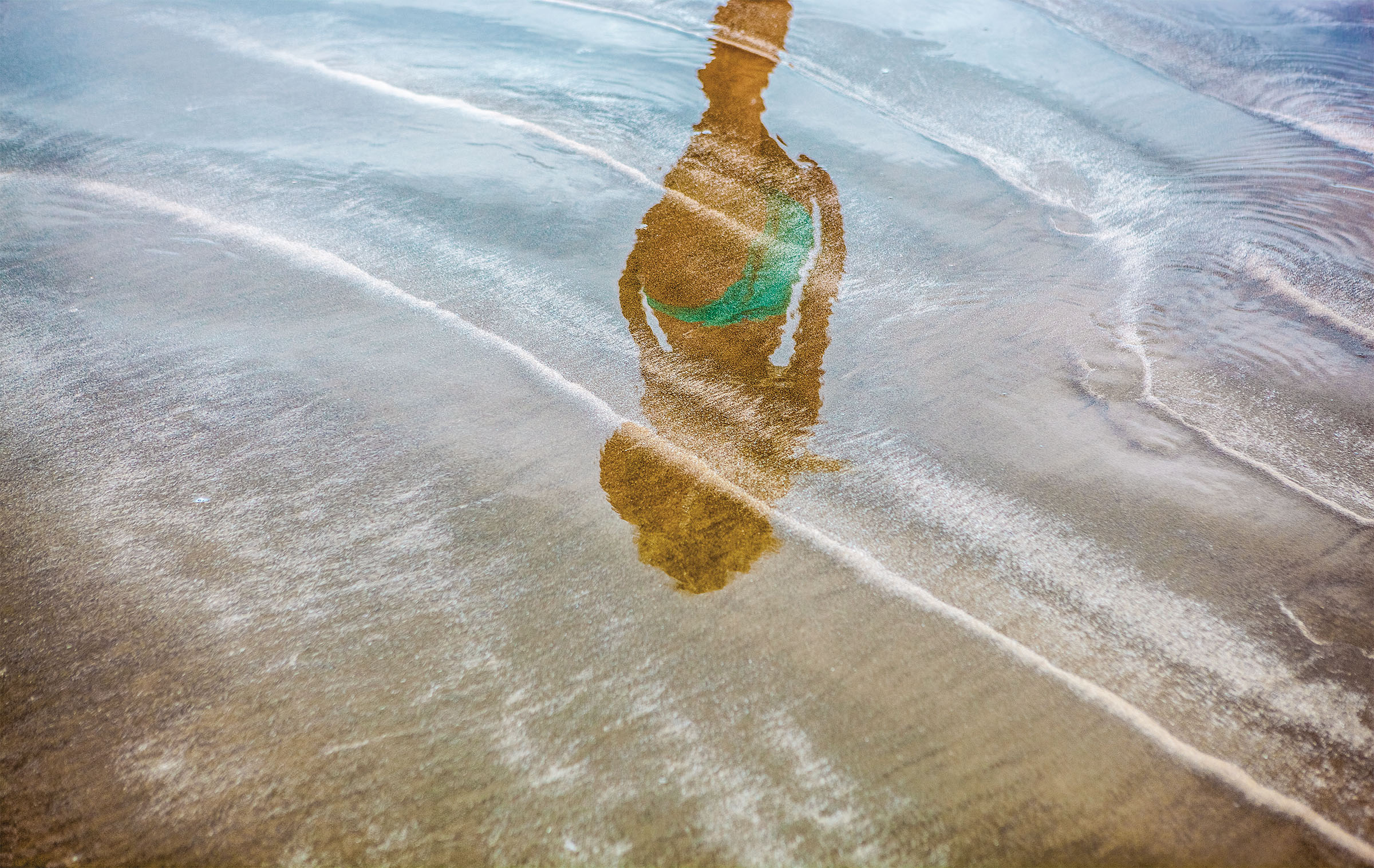 The reflection of a person walking the beach in a swimsuit