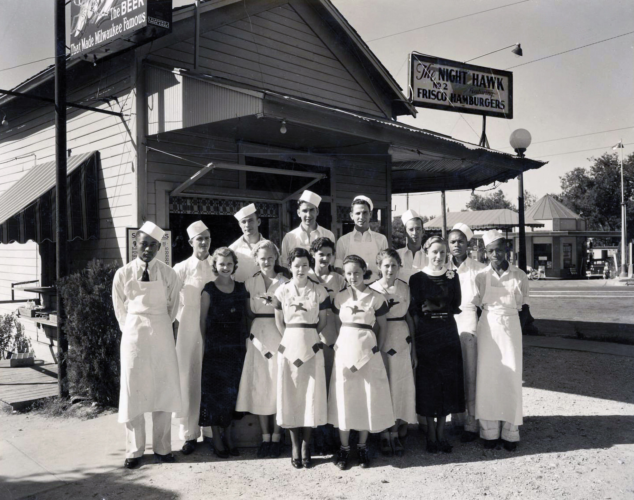 A group of people dressed in crisp white uniforms stand outside of a building in a black and white picture