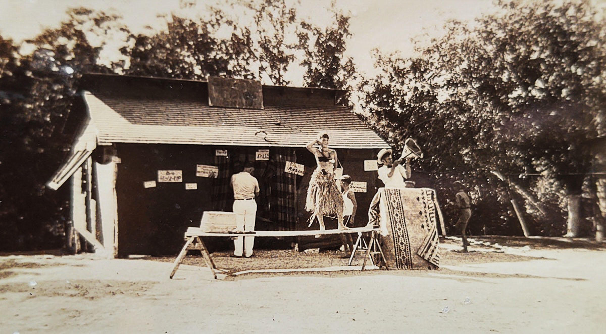 A sepia-tone image of people standing in front of an wooden building in costume