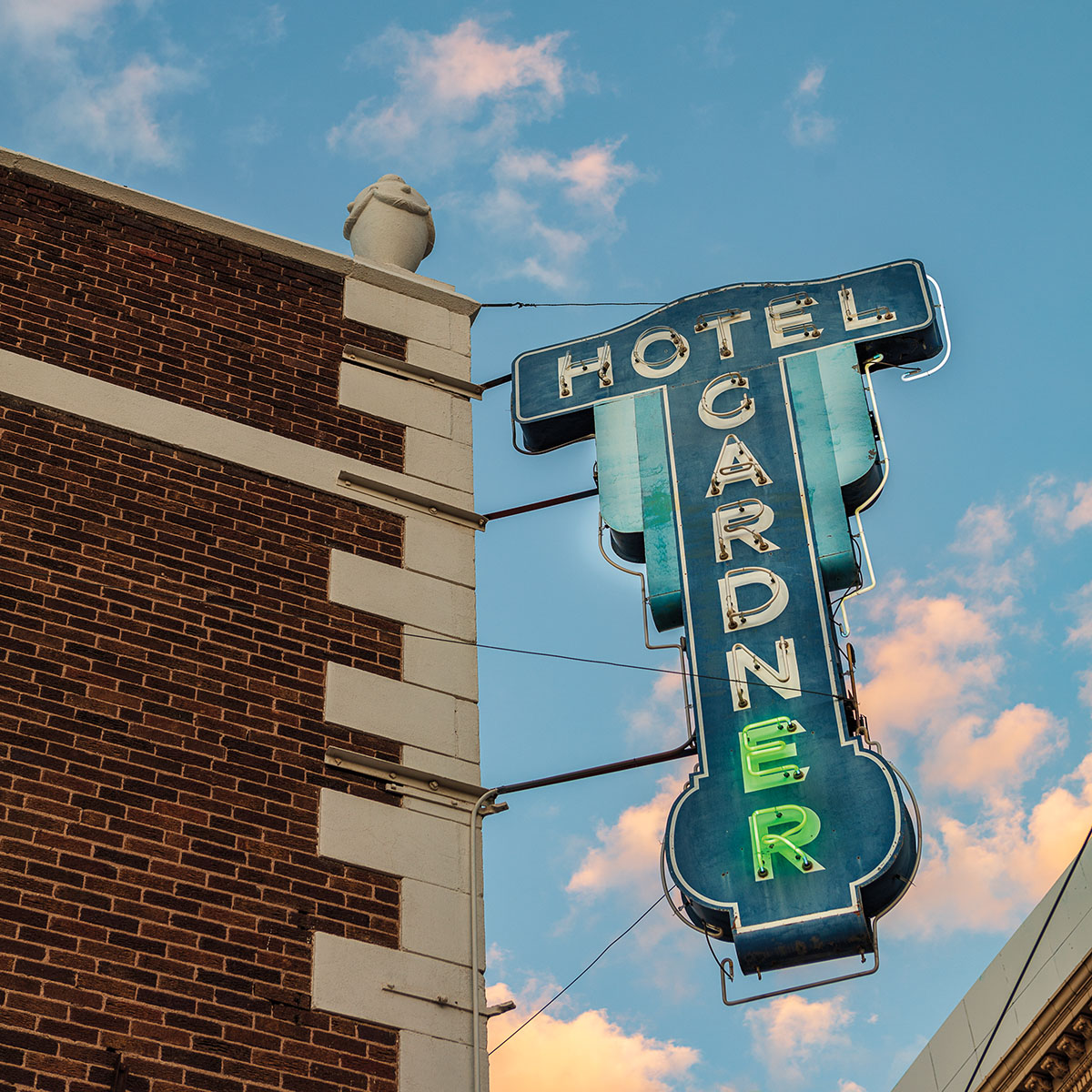 A green-blue sign reading "Hotel Gardner" is partially illuminated in front of a blue sky with a few clouds