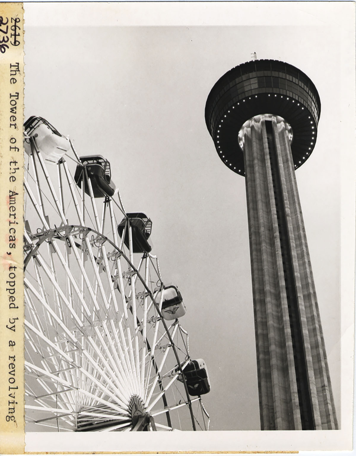 A tall tower with a black top next to a white and black Ferris wheel in a historic photograph
