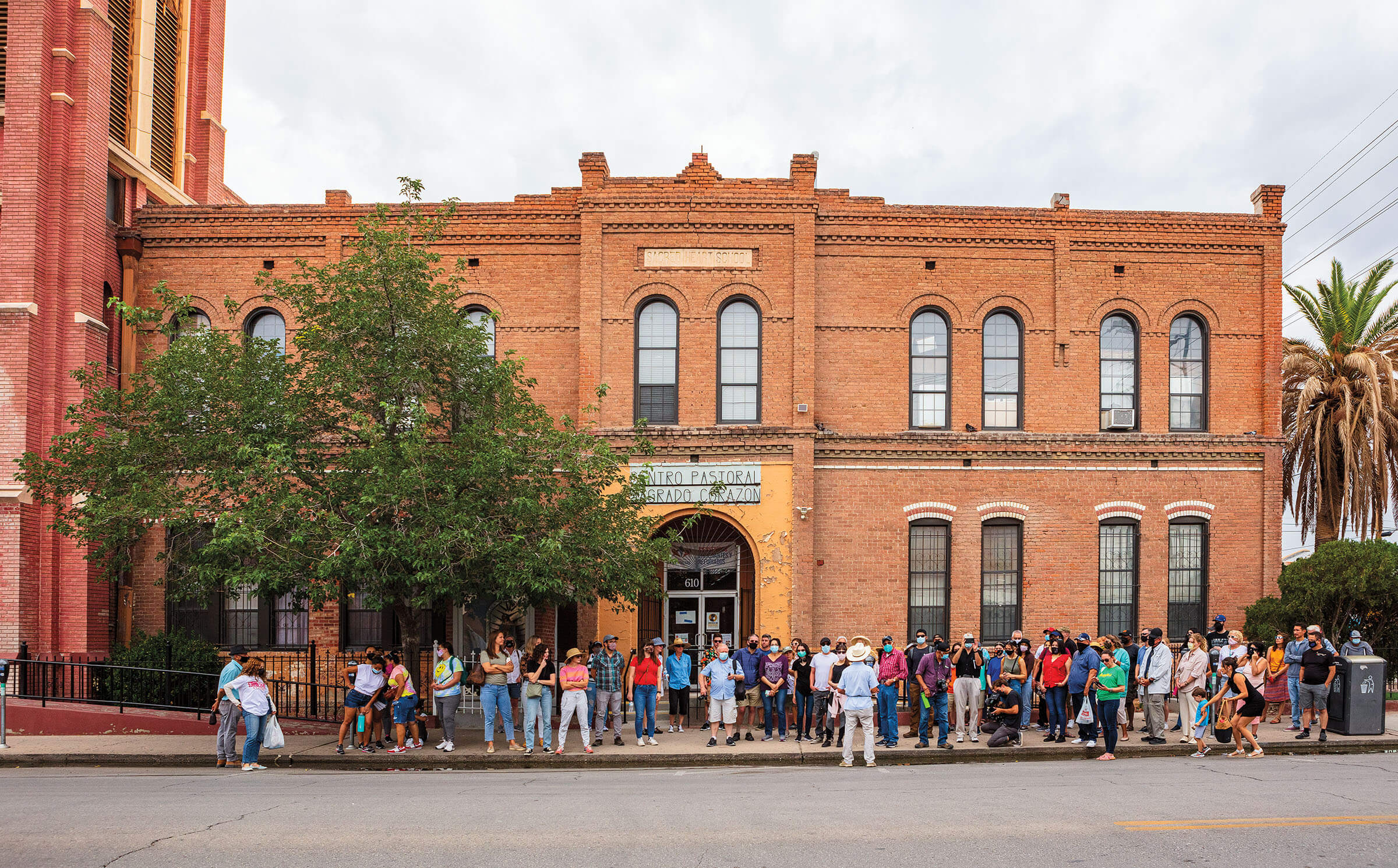 A large group of people stand out front of a brick building with old curved windows