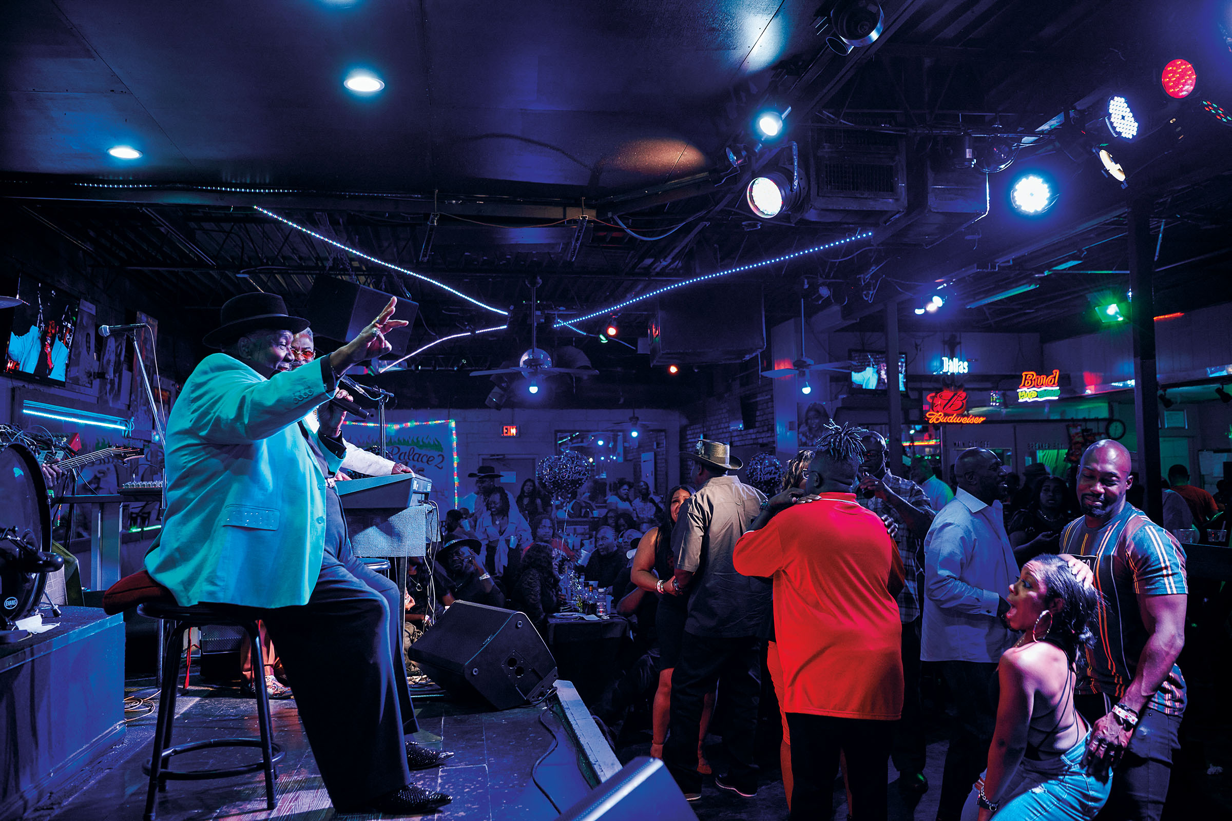 People dance in the crowd next to a man in a blue sport coat performing in a dark club