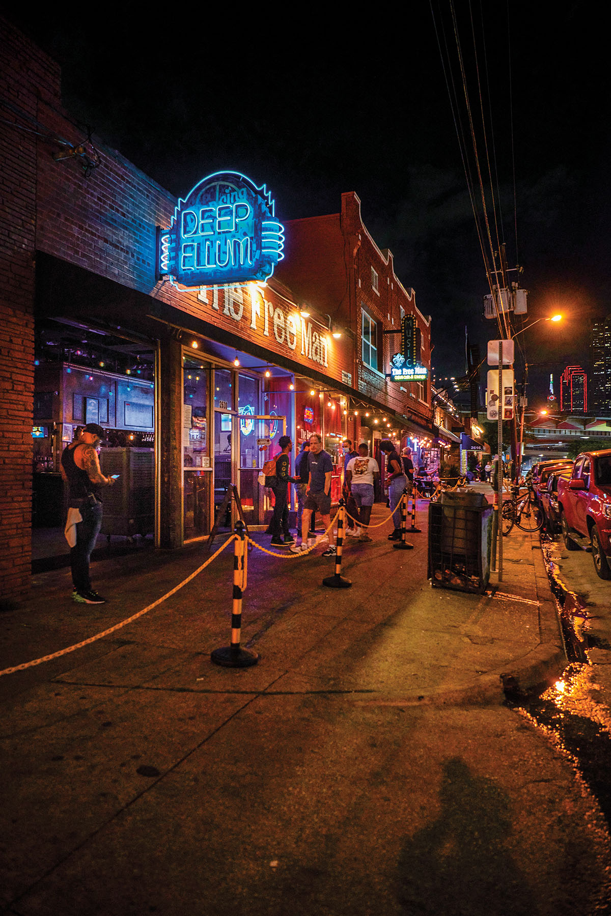 A nighttime scene of a blue neon sign reading "Deep Ellum" with people walking on the street below