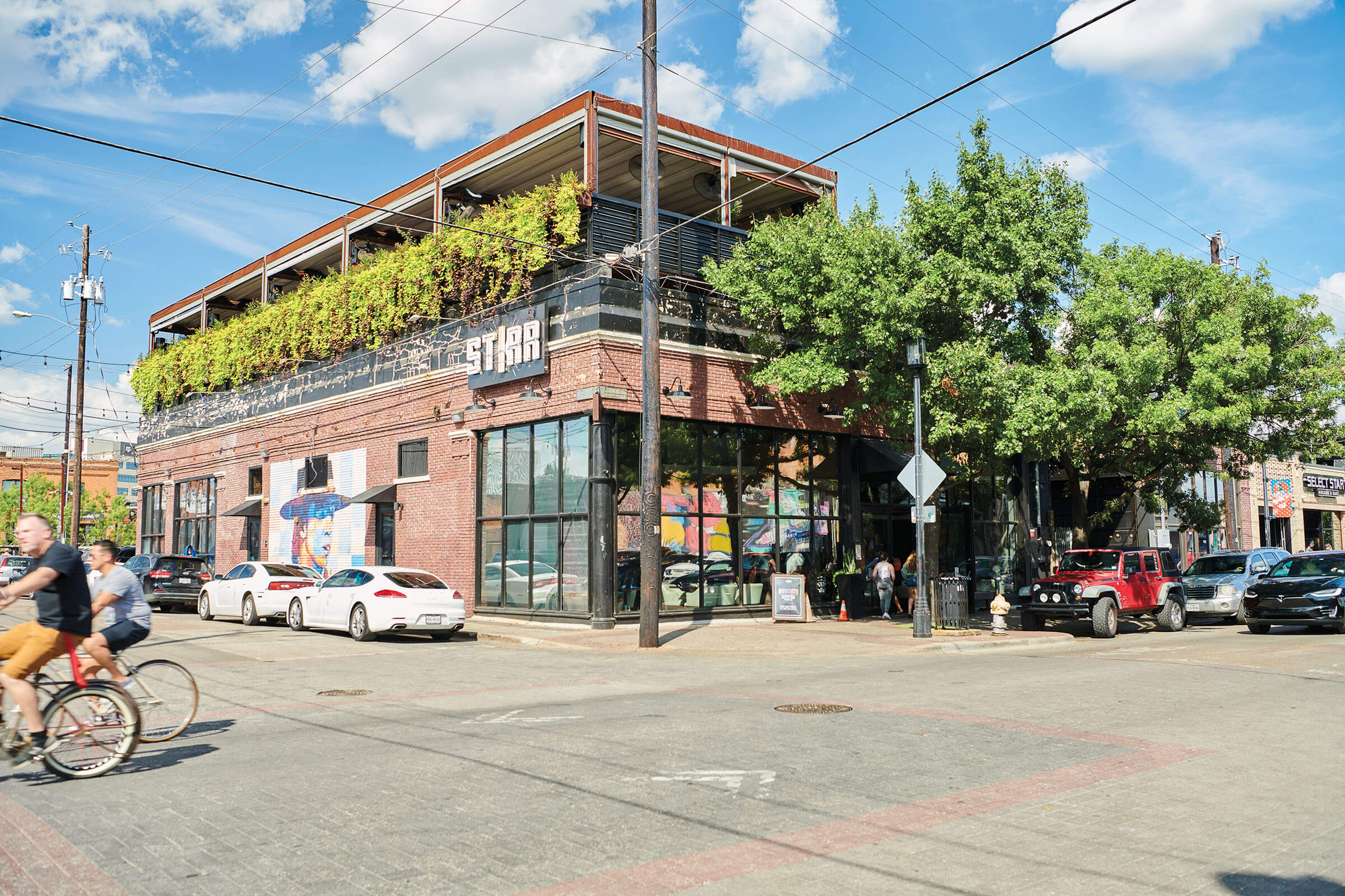 The outside of a brick building reading "STIRR" on the outside with a handful of cars parked on the street in front