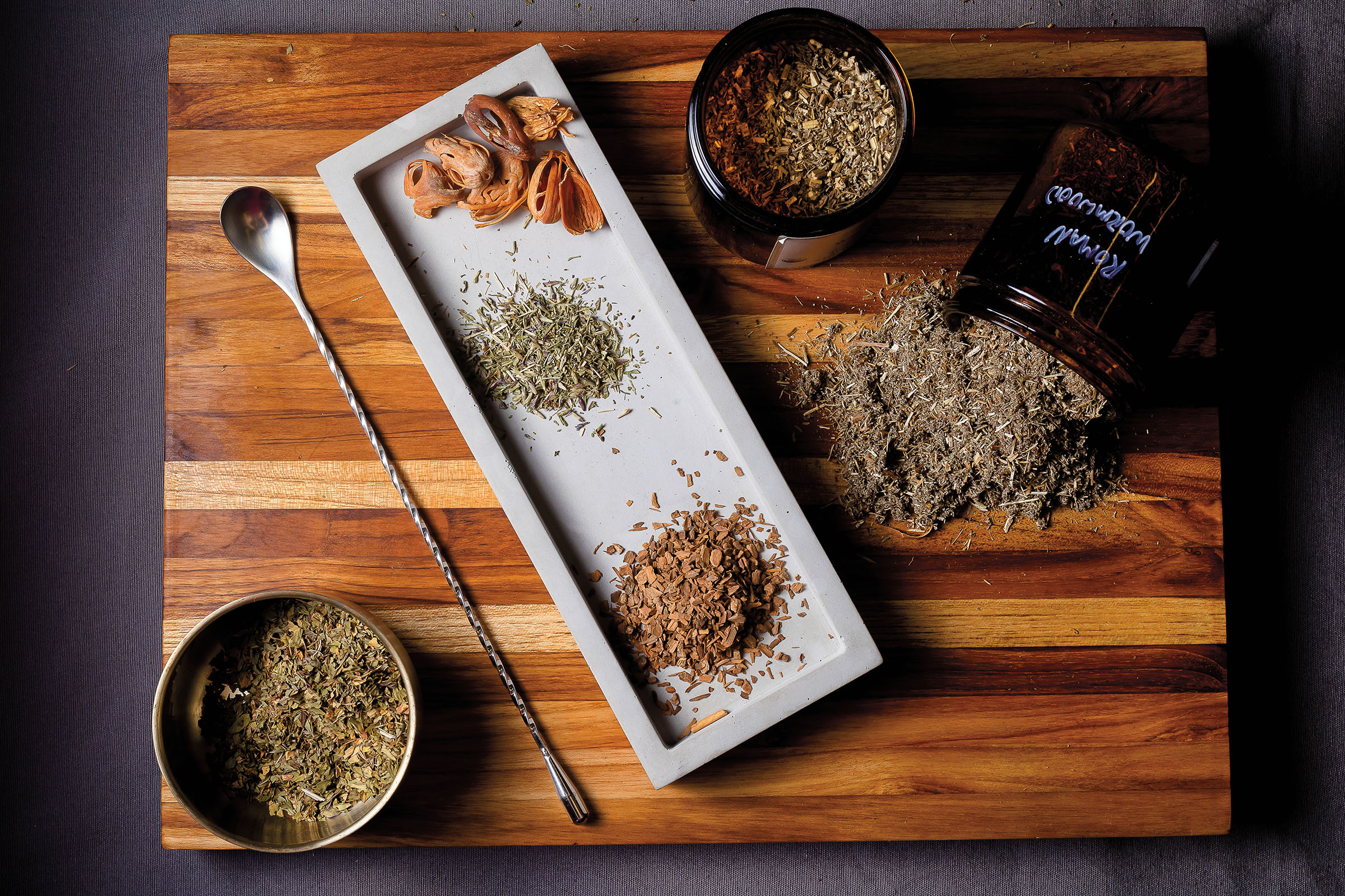 An overhead view of a plate with herbs and flowers laid out. Three dark glass jars are open next to the tray with their contents spilled on a wooden cutting board