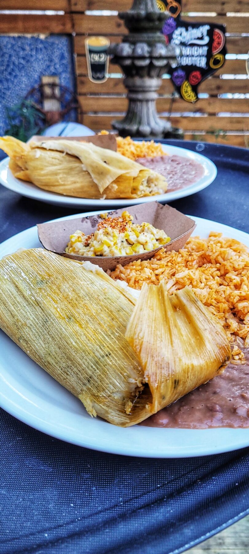 tamales on a plate with a side of rice and refried beans on an outdoor patio