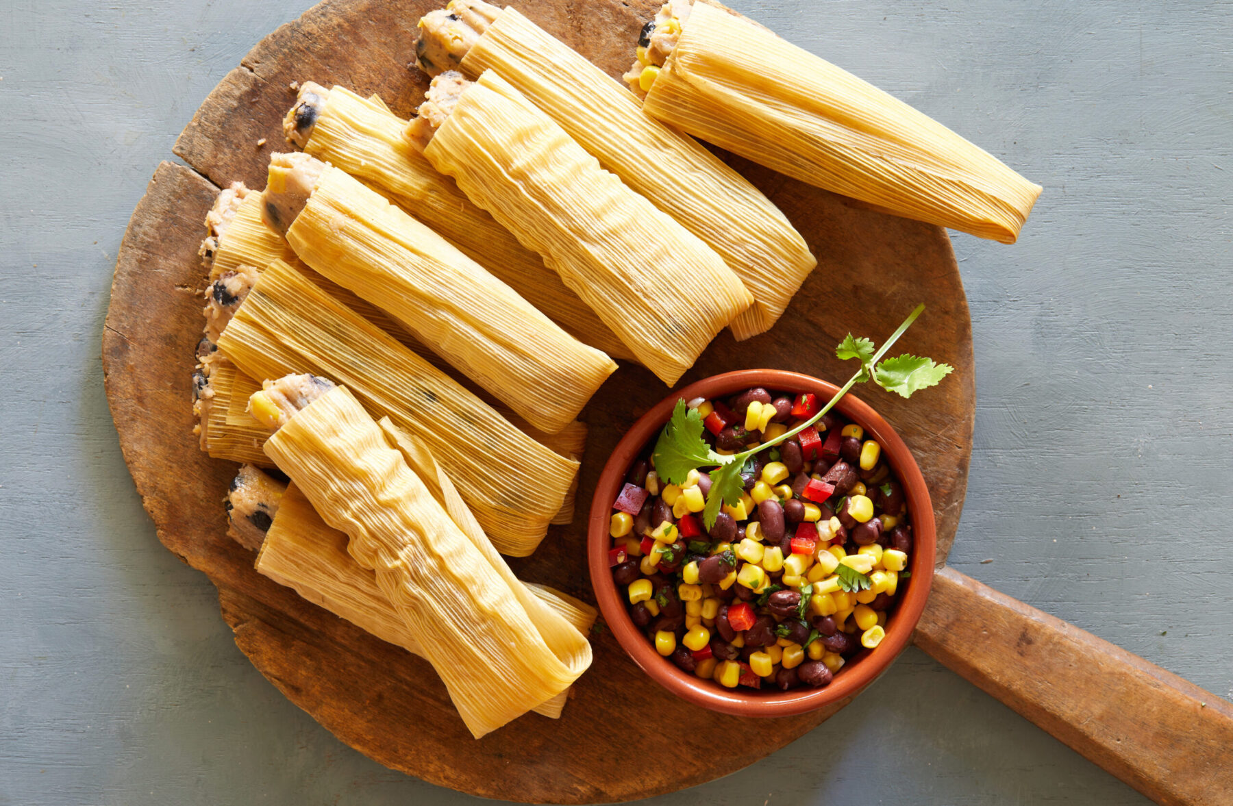 several tamales on a wood board with a side of salsa in a bowl
