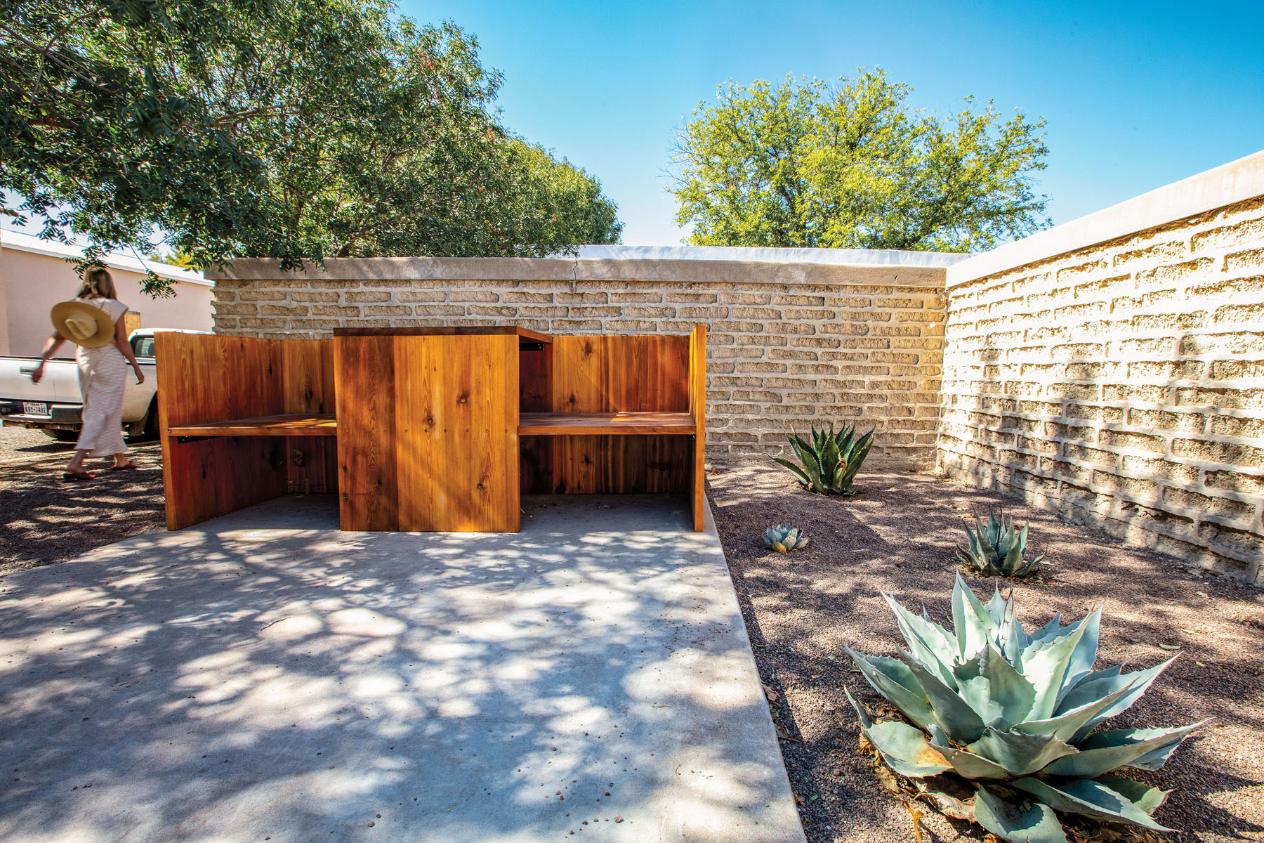 Pointy agave grow in a gravel garden bed next to a slab of concrete and stained wooden panels