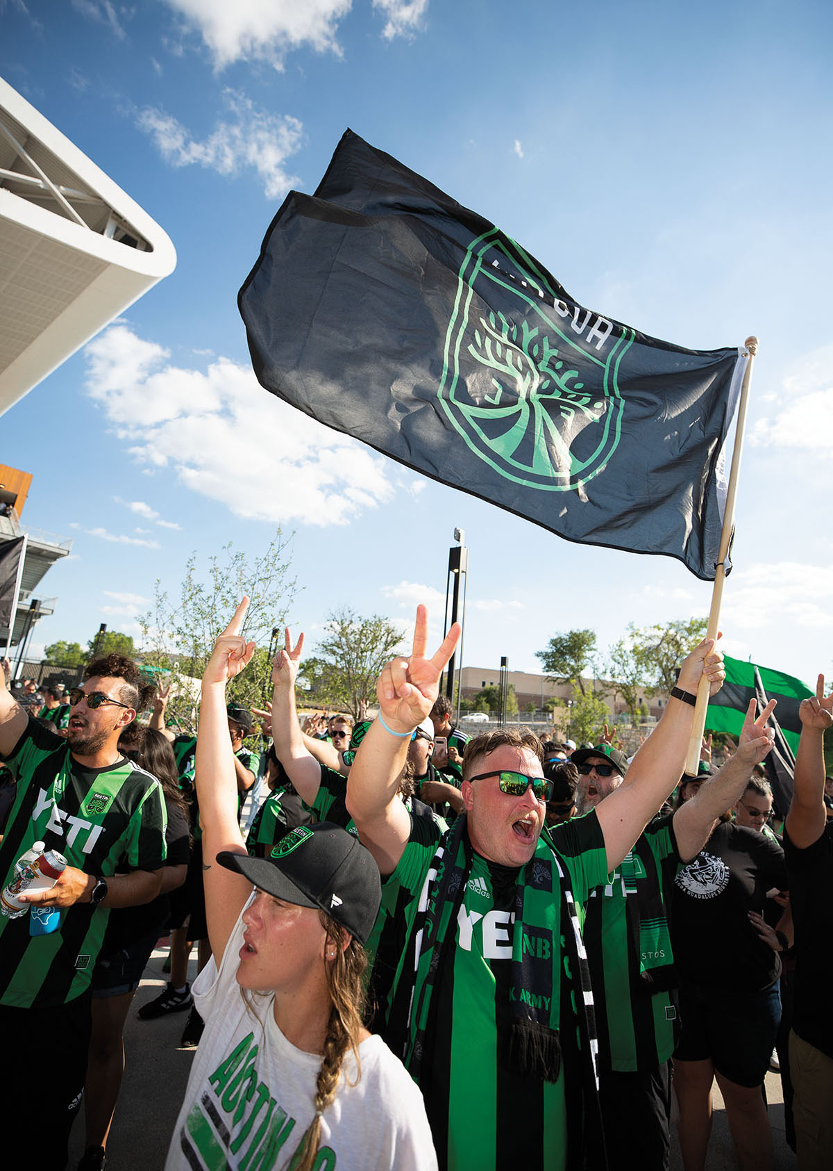 A group of fans wave a large Austin FC flag with a green tree and Verde logo