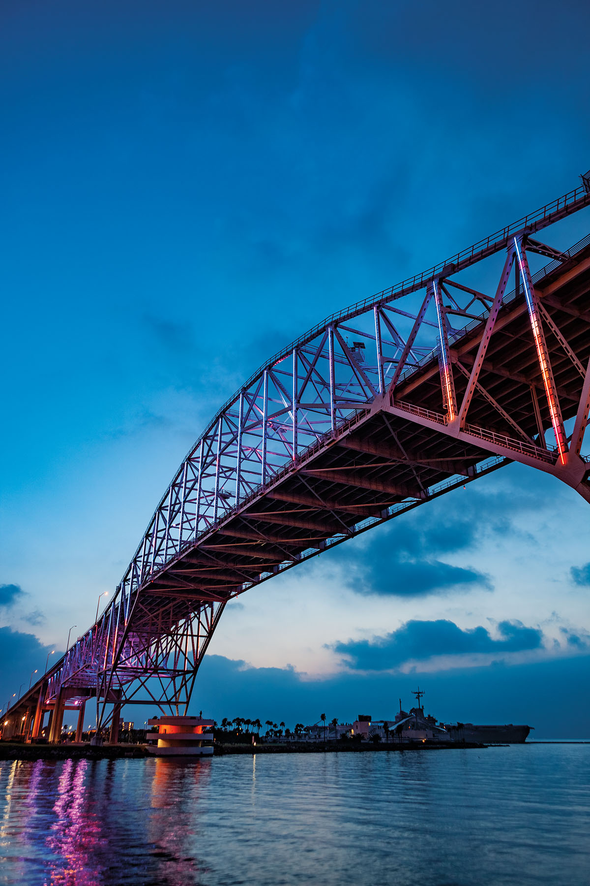 A large steel bridge in front of a dark blue sky illumited by soft purple lights