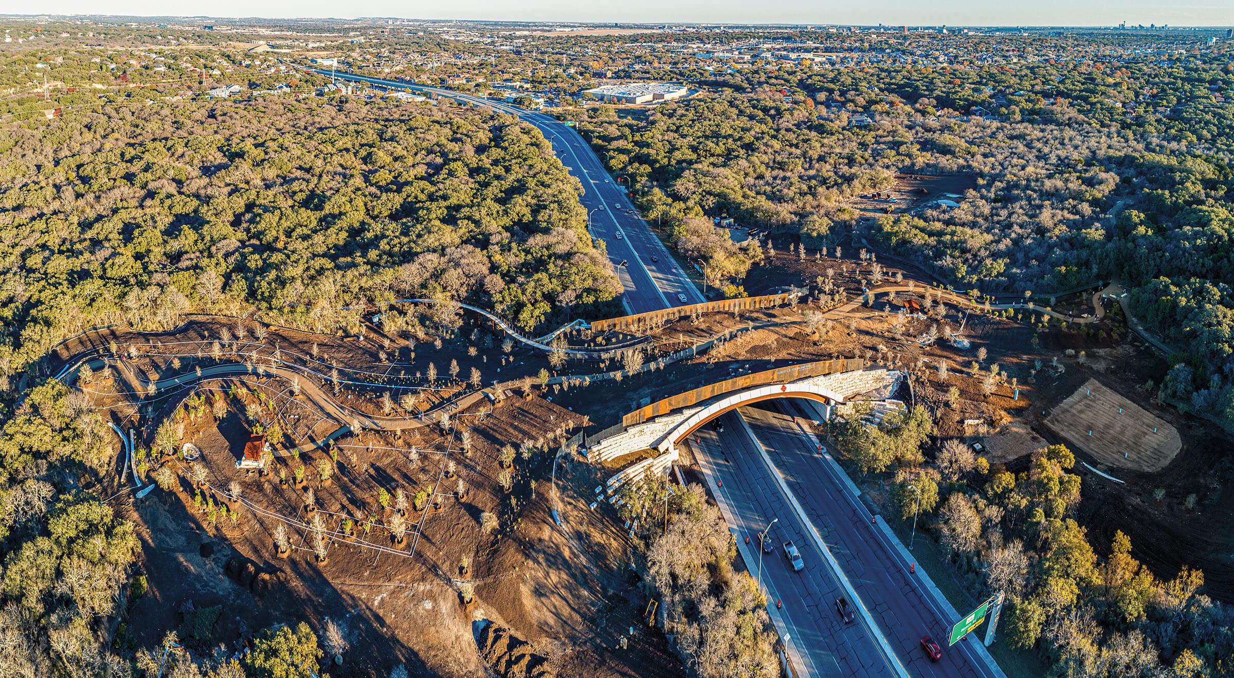 A land bridge being constructed over a road with large green trees on either side
