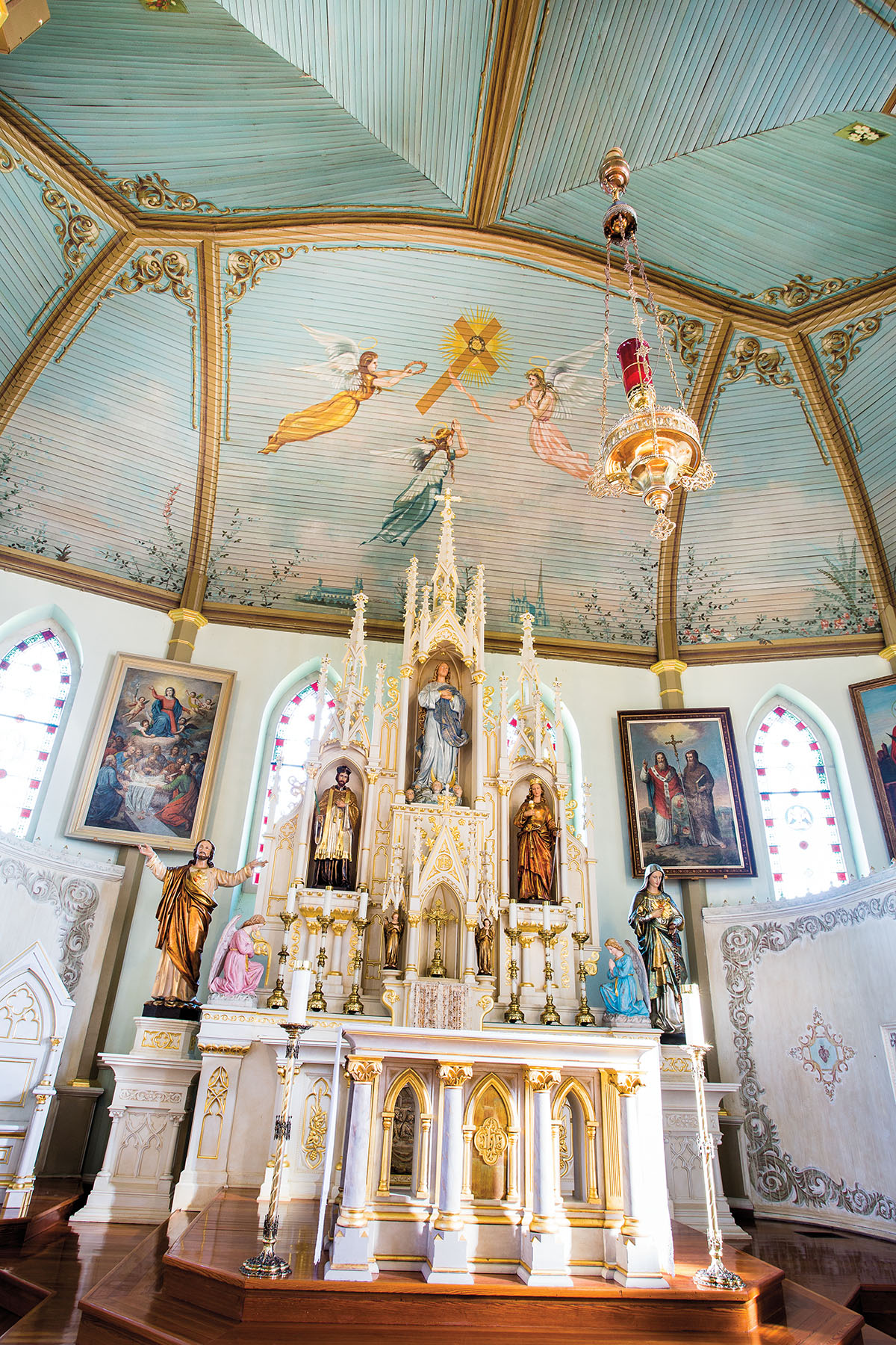 The interior of a beautifully painted cathedral, complete with a blue sky, flying angels, a large white altar, brightly-colored statues, and stained glass