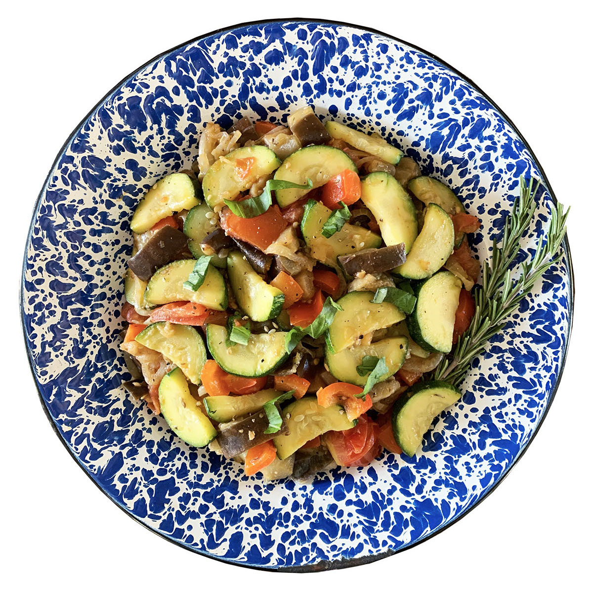 An overhead view of a blue and white plate of multi-colored and vegetable-heavy ratatouille