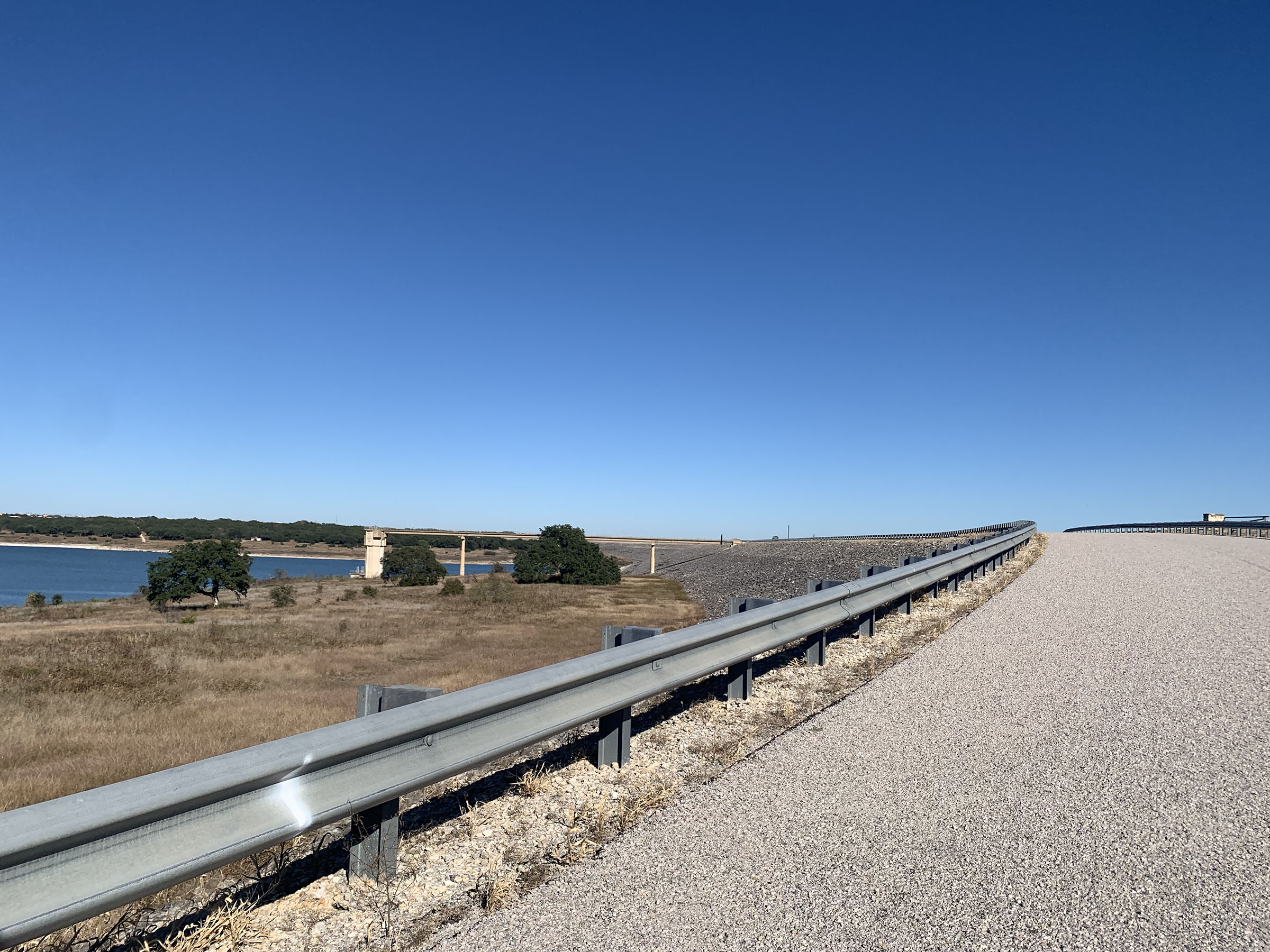 A steel guardrail next to a wide gray road under blue sky