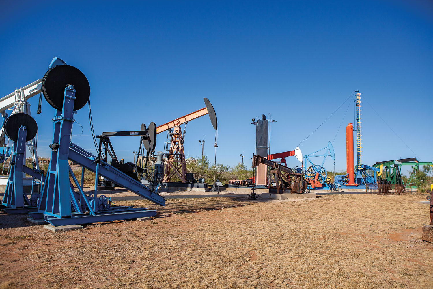 A collection of colorful pumpjacks and other oil drilling equipment on a brown grass field