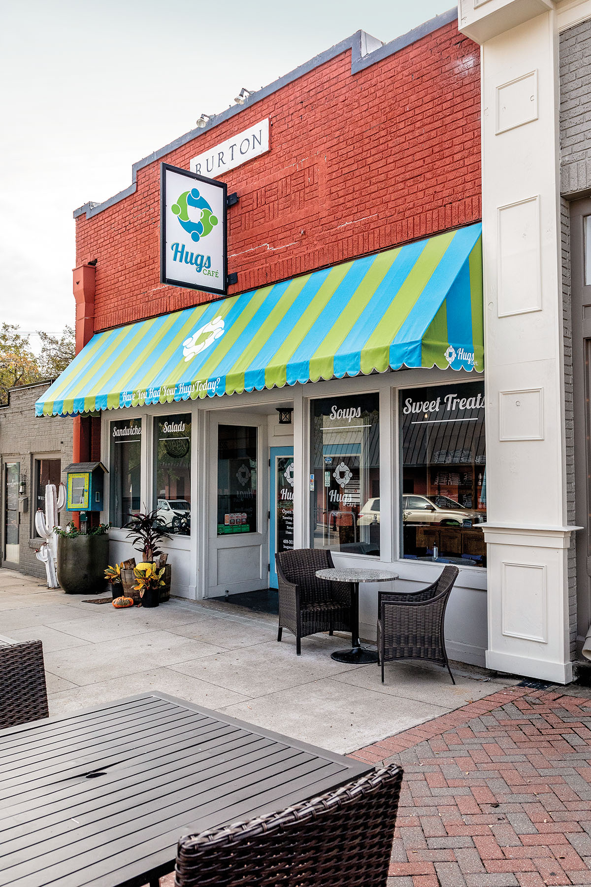 A bright blue and green-striped awning adorns the outside of a red brick building with a sign reading "Hugs Cafe"
