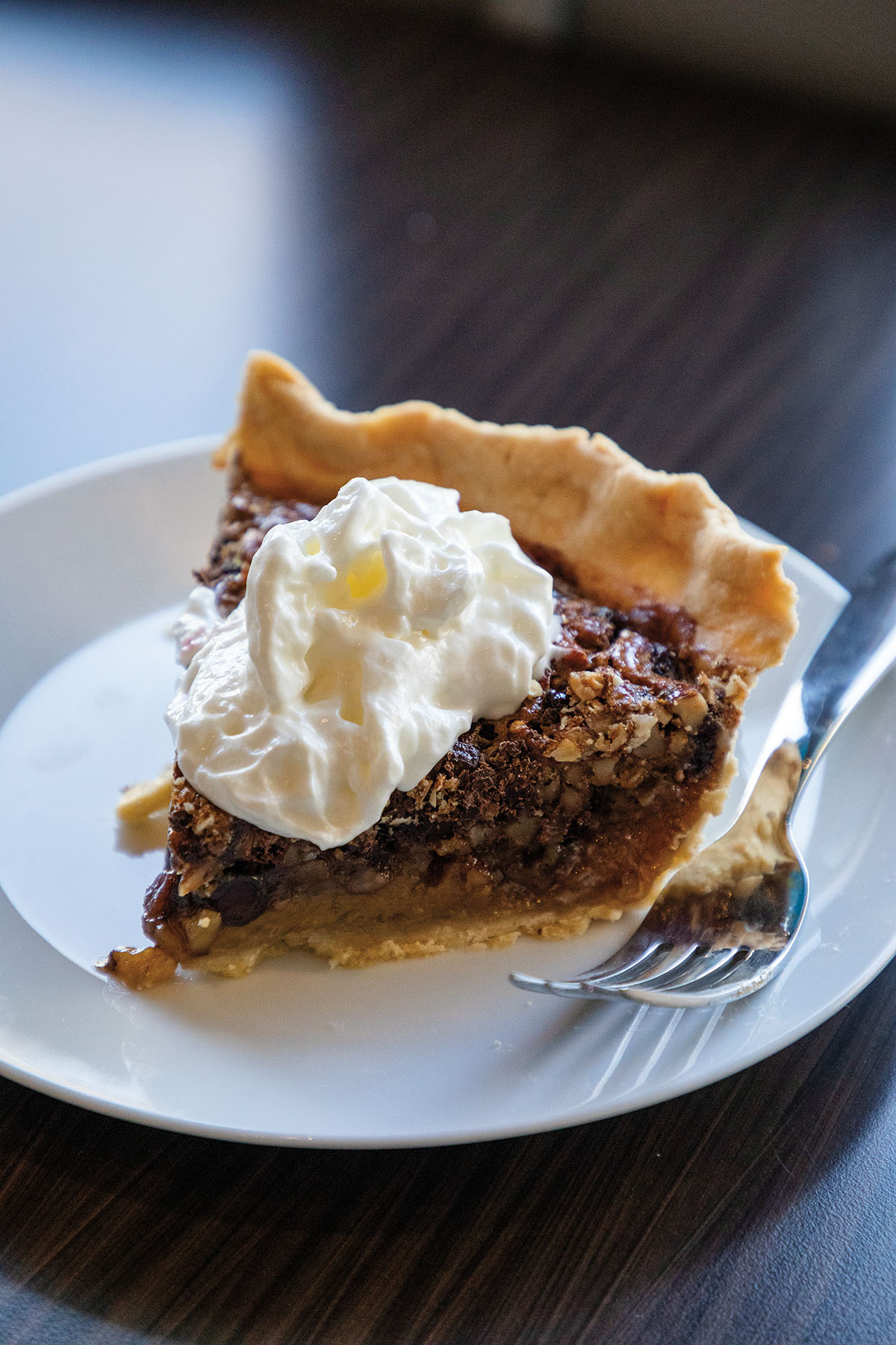 A slice of pecan pie on a white plate topped with whipped cream
