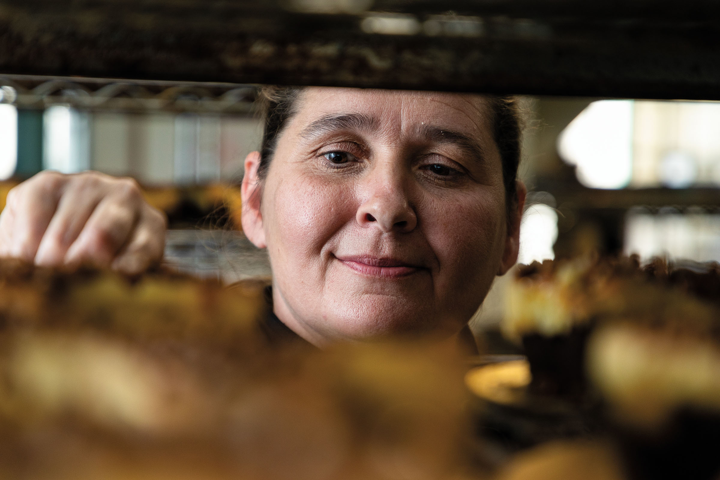 A woman peeks through racks of cheesecake with a slight smile