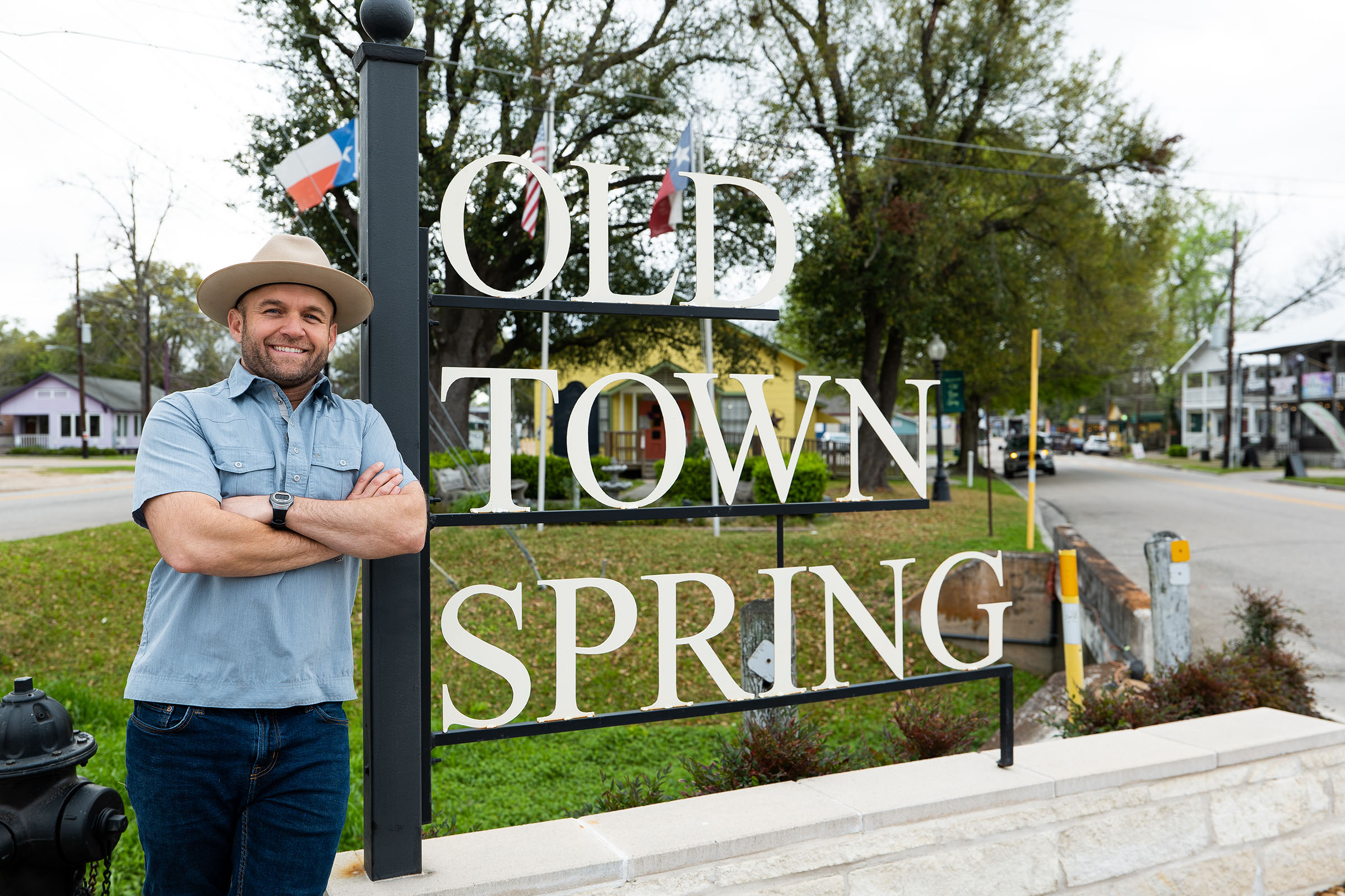 A man in a cowboy hat leans against a metal sign reading "OLD TOWN SPRING"