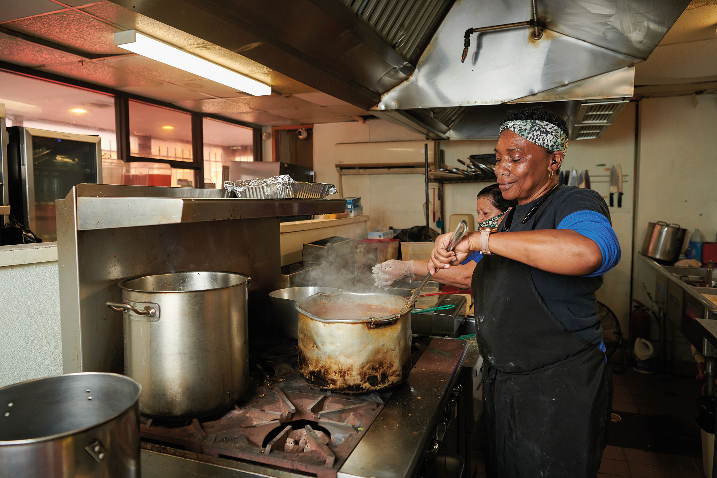 A woman in a kitchen stirs a steaming pot in a kitchen