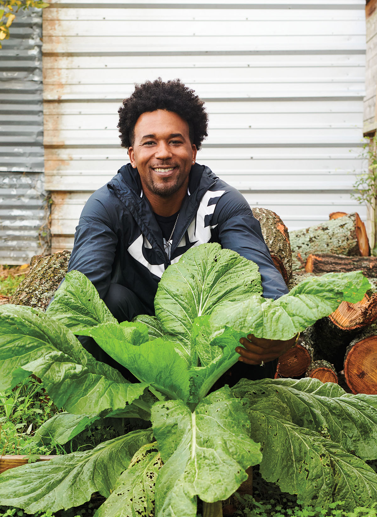 A man in a blue sweatshirt sits behind a large, leafy green plant outdoors