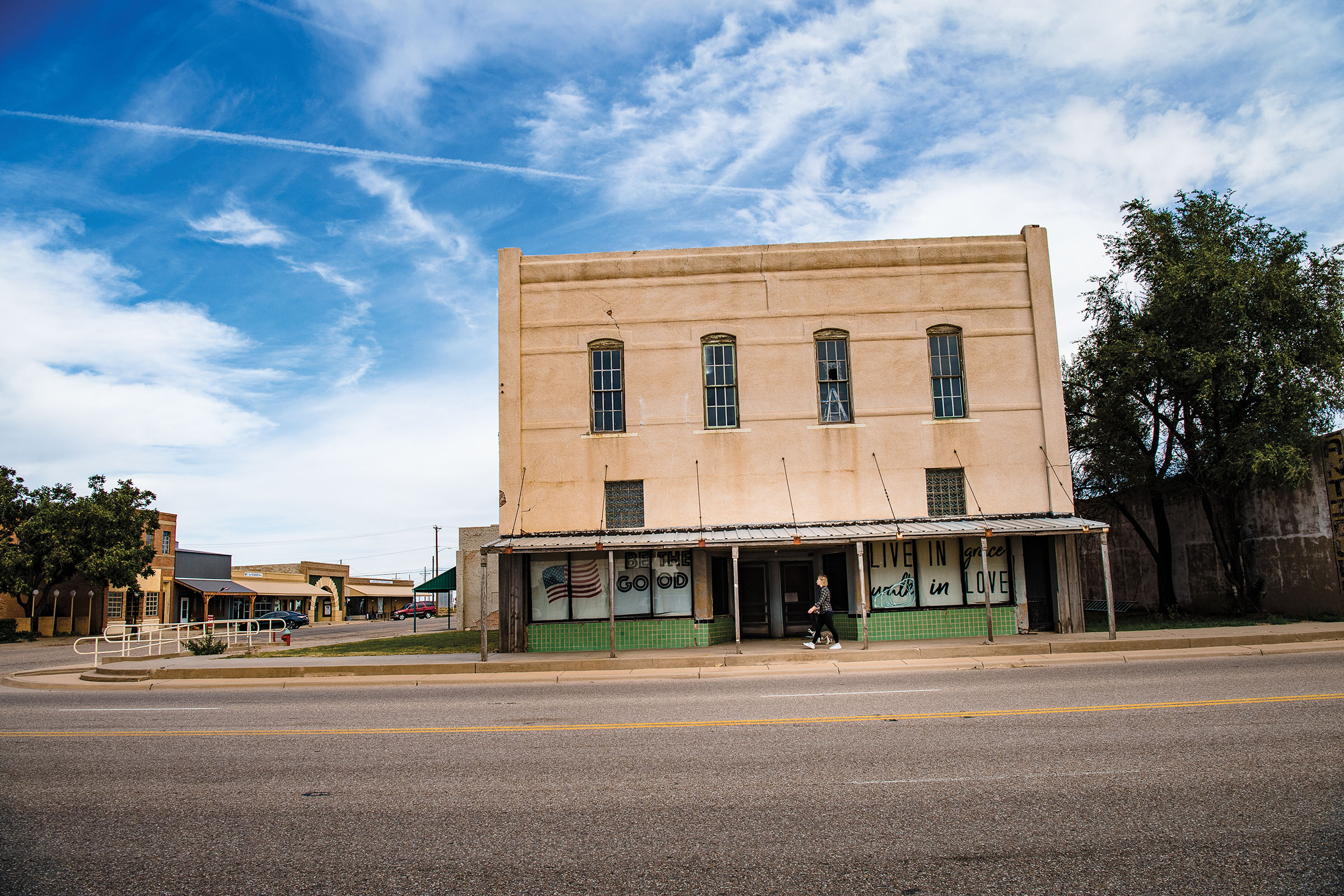 A faded brick building along the side of a road under blue skies with clouds