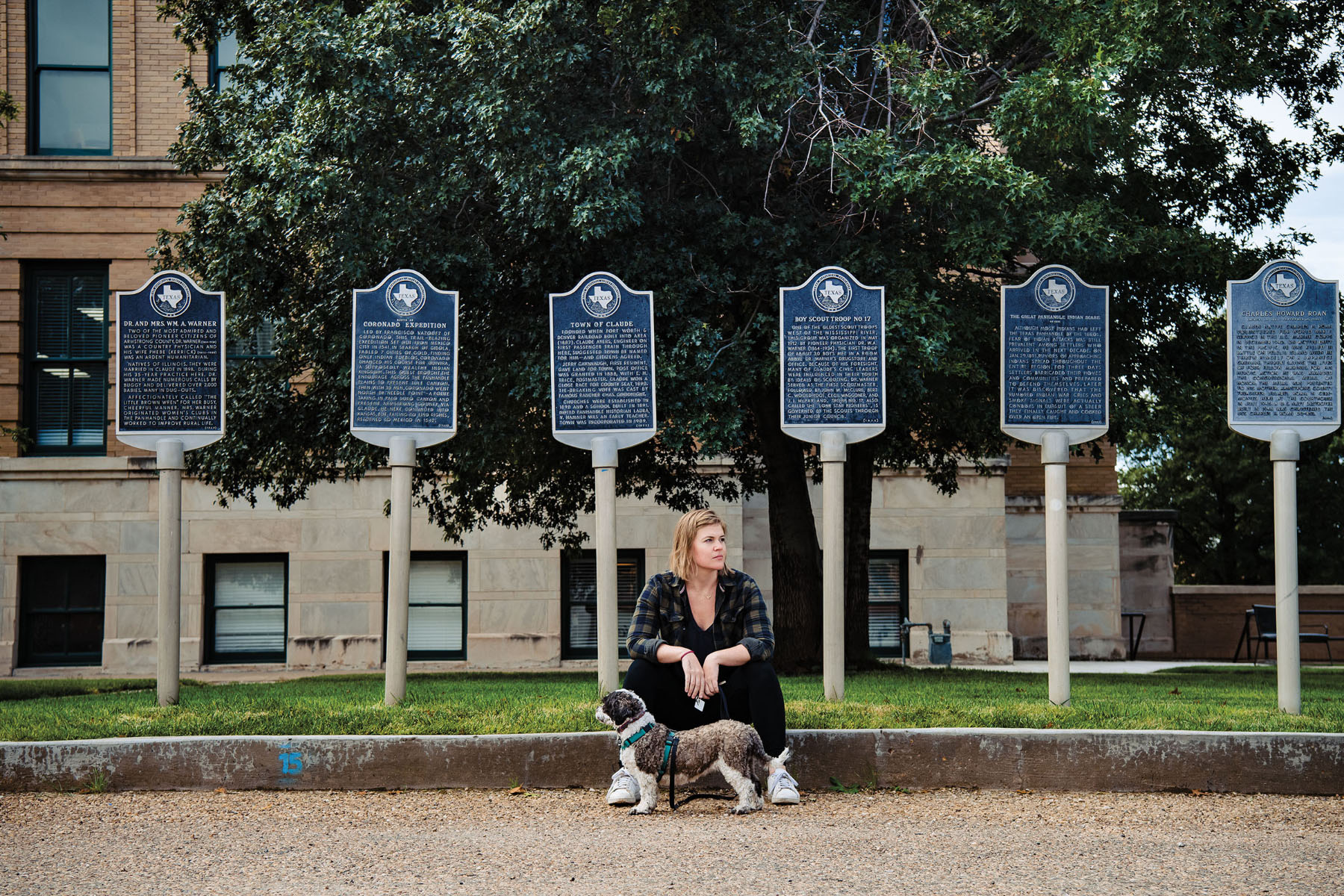 A woman sits on the curb in front of a collection of Texas historical markers