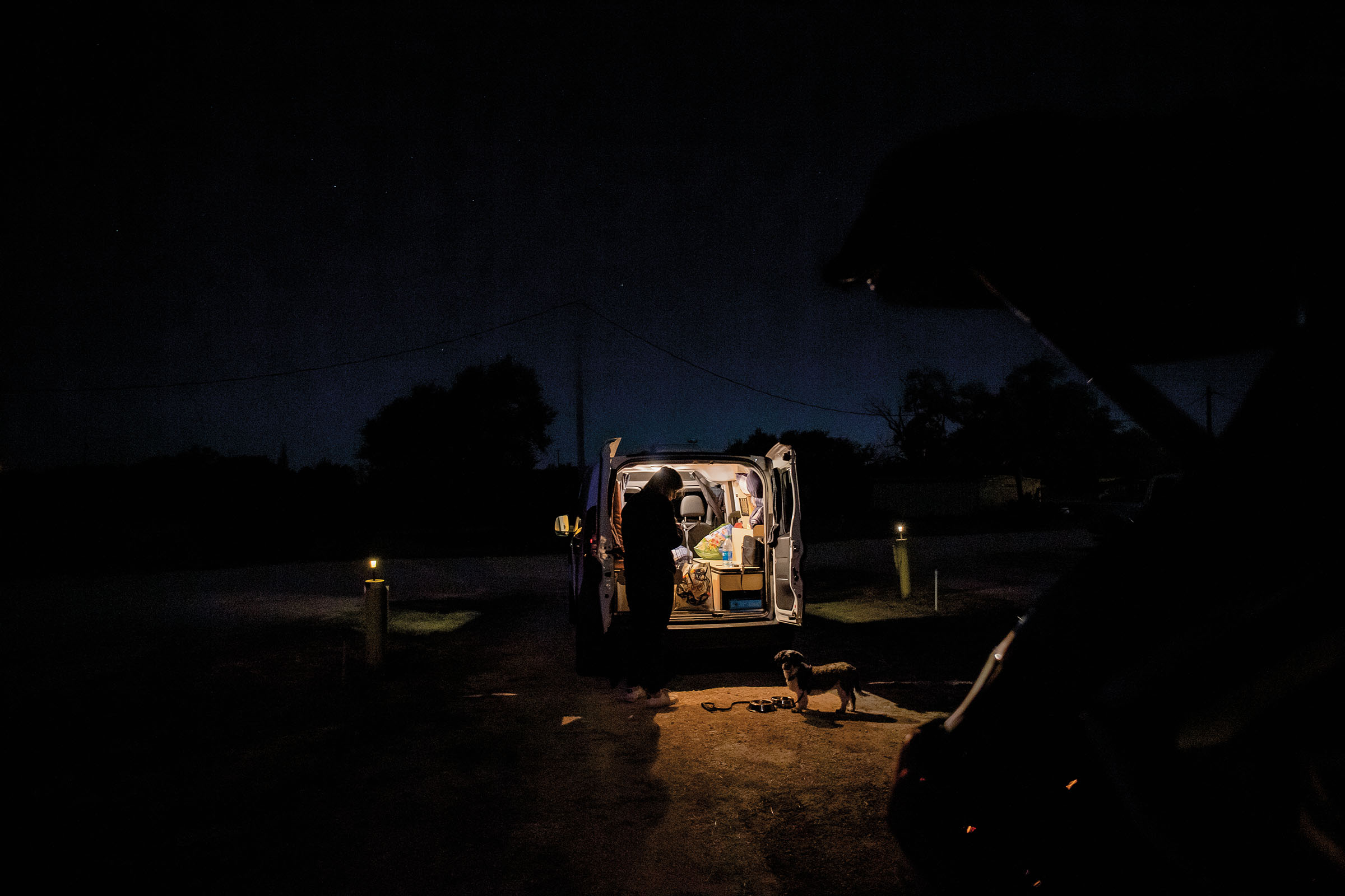 The author stands in the light of her van talking to the dog, Cleo, who stands on the ground dimly lit