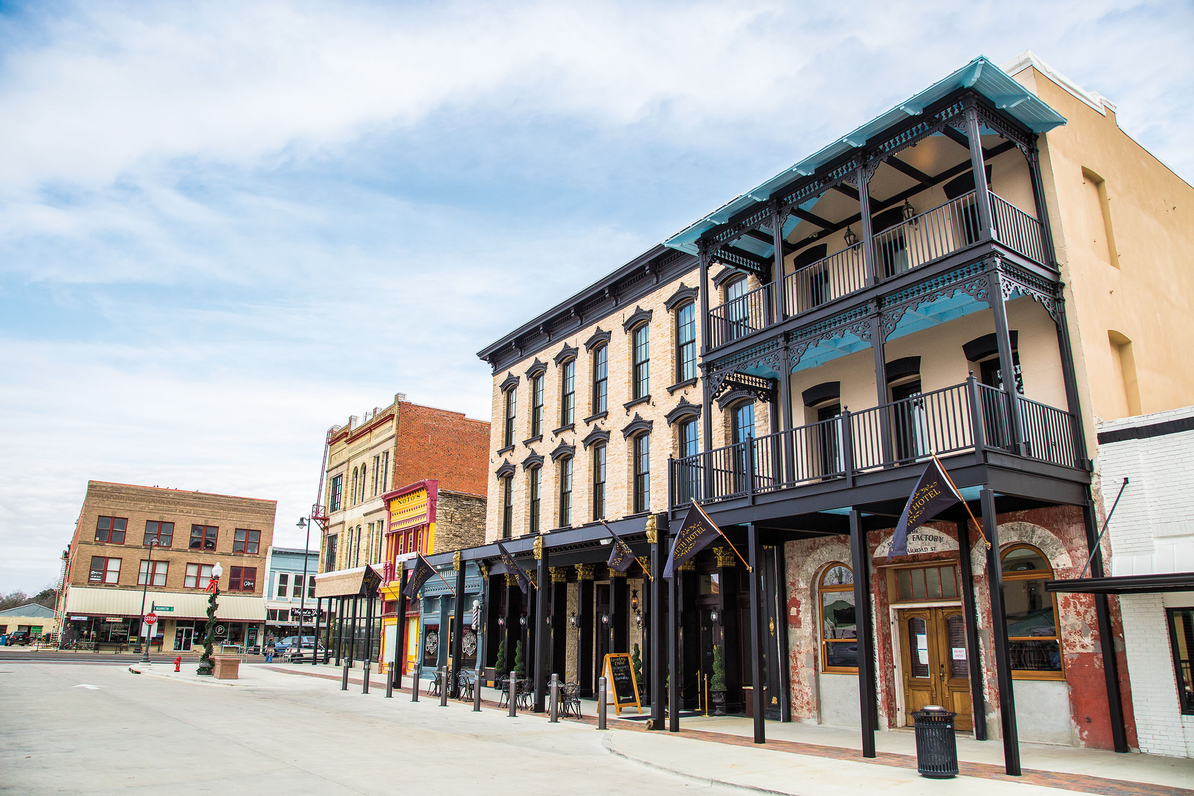 A collection of neatly maintained buildings on a downtown street, including a historic hotel with a stone facade and black painted trim