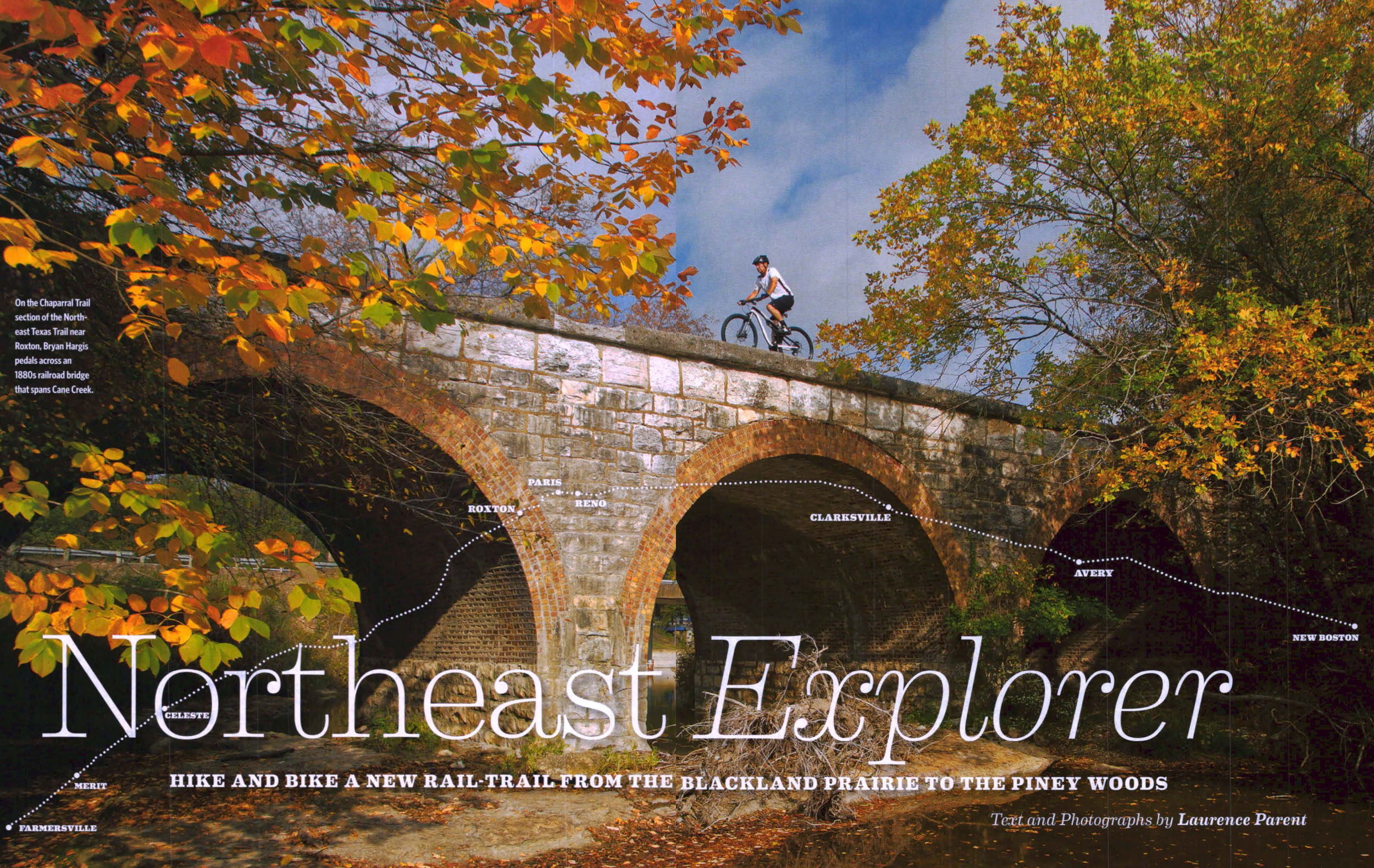 A person rides a bike over a stone bridge surrounded by fall colors