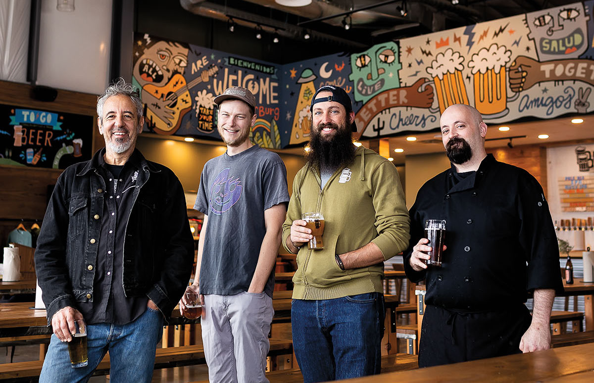 A group of men stand, three of them holding pints of beer, in a brightly-painted brewery