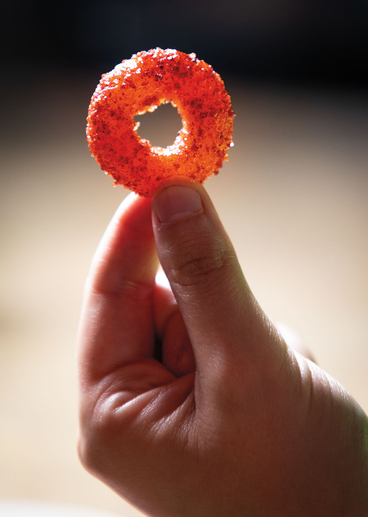 A hand holds up an orange-pink candy coated in bright red seasoning
