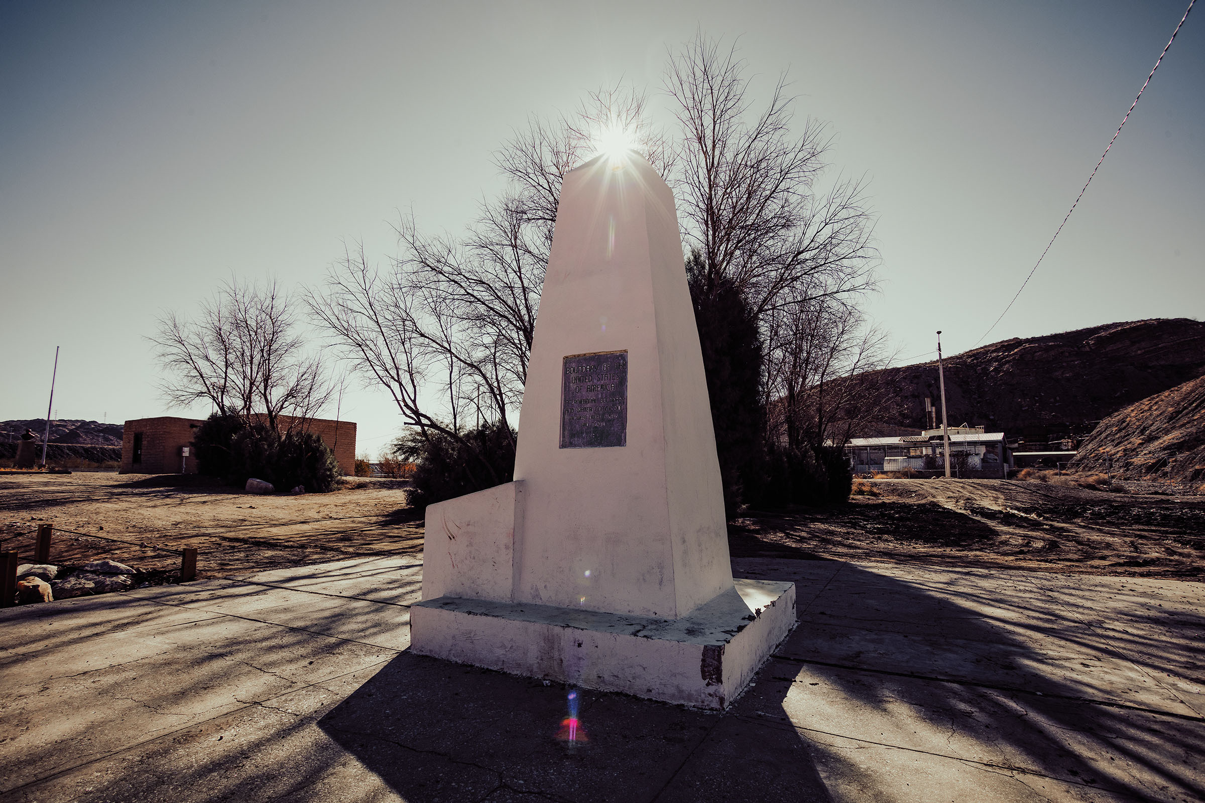 The sun shines behind the top of a concrete obelisk in a desert landscape