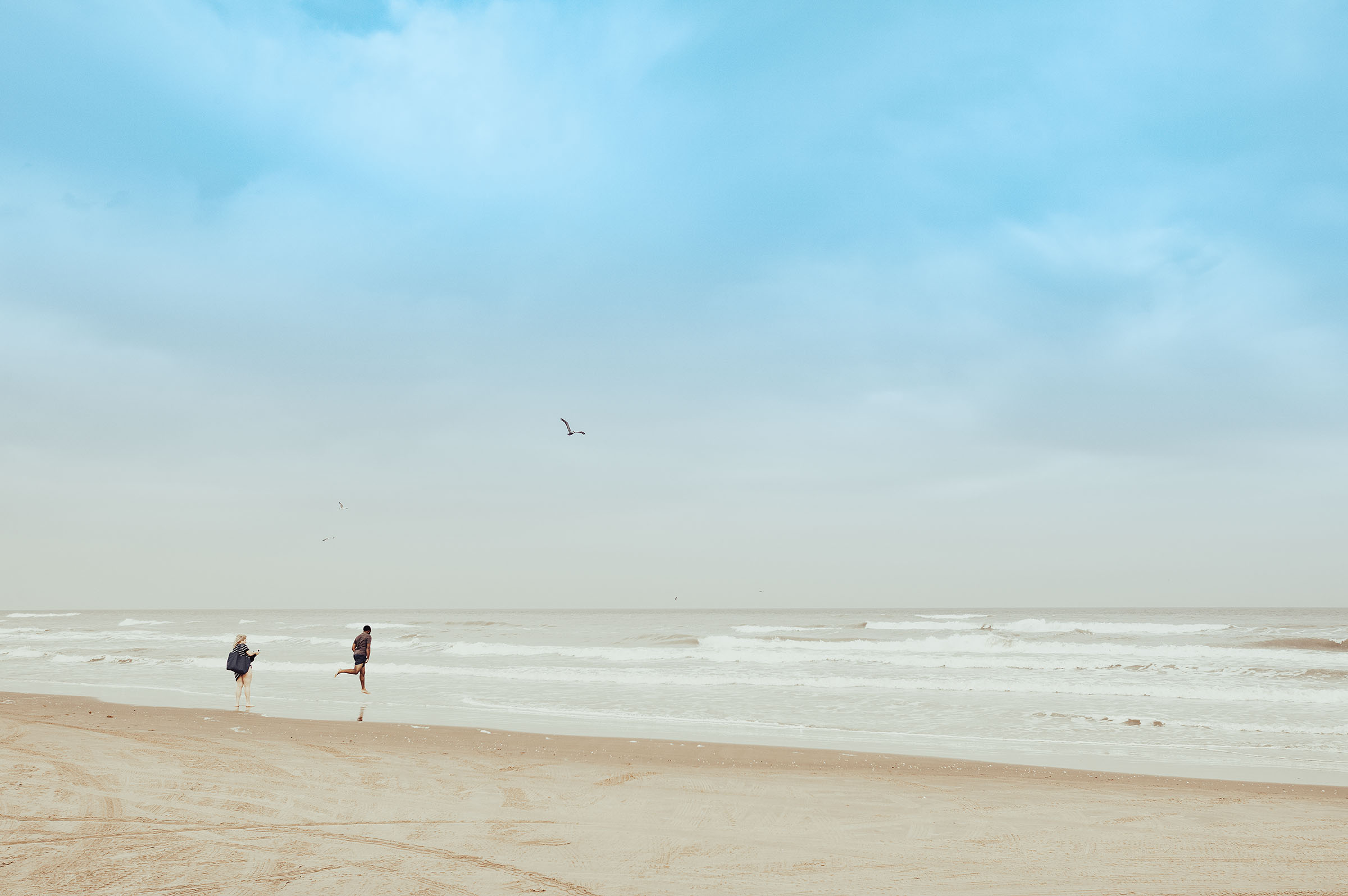 People run into the water along a clear beach under bright blue sky