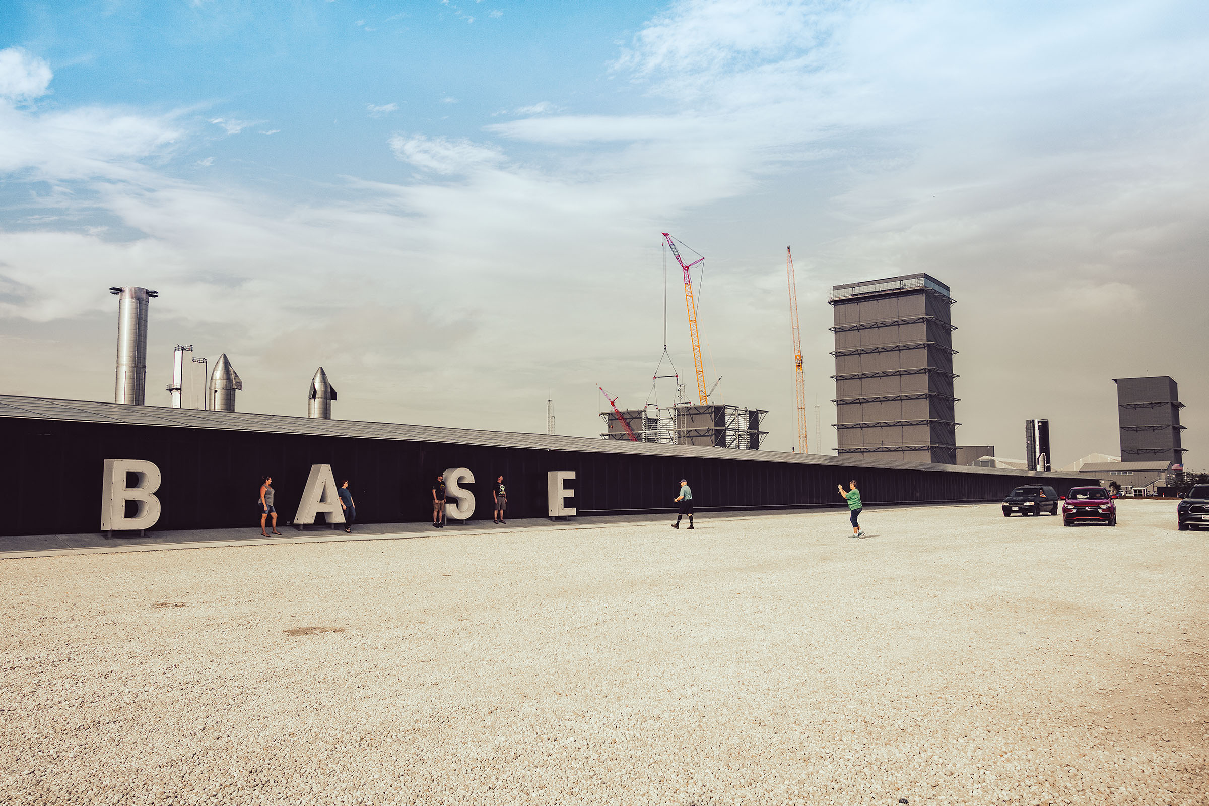 A small group of people pose in front of letters reading "BASE" with several tall cranes