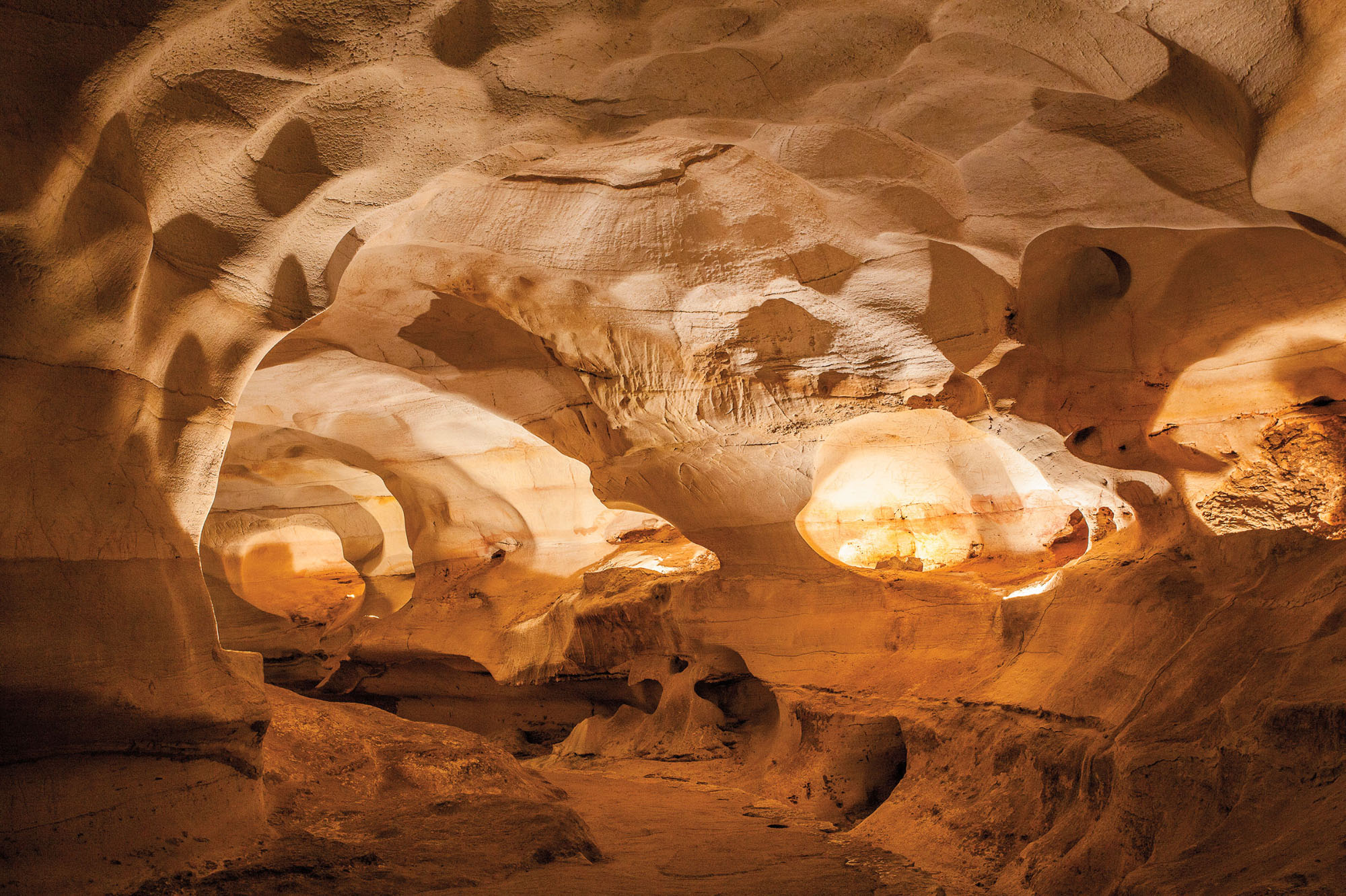 An image of a golden-tan cave lit up to show the large and various caverns and spaces within
