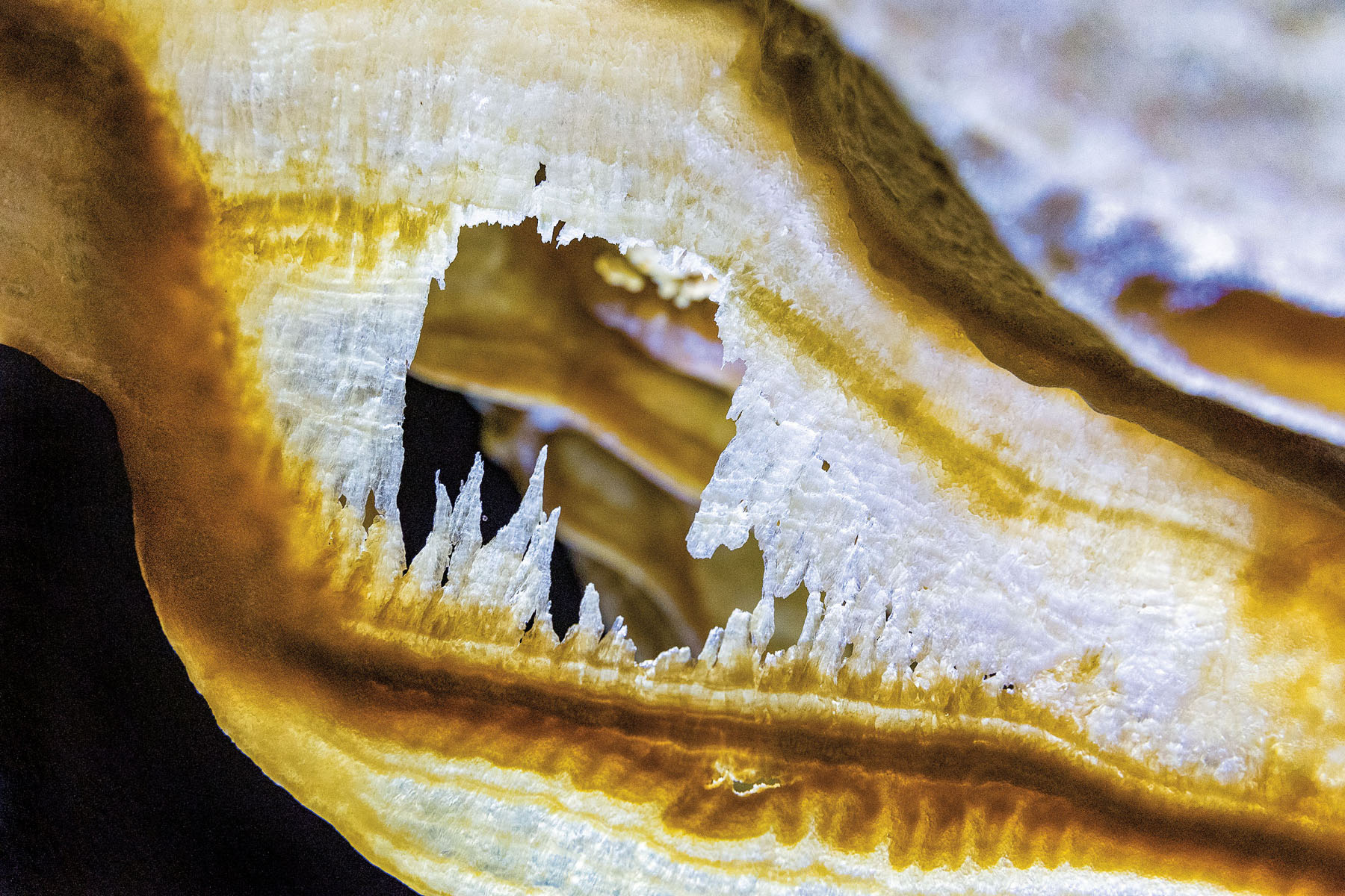 A white and golden-striped rock formation with spiny white points inside of an open space