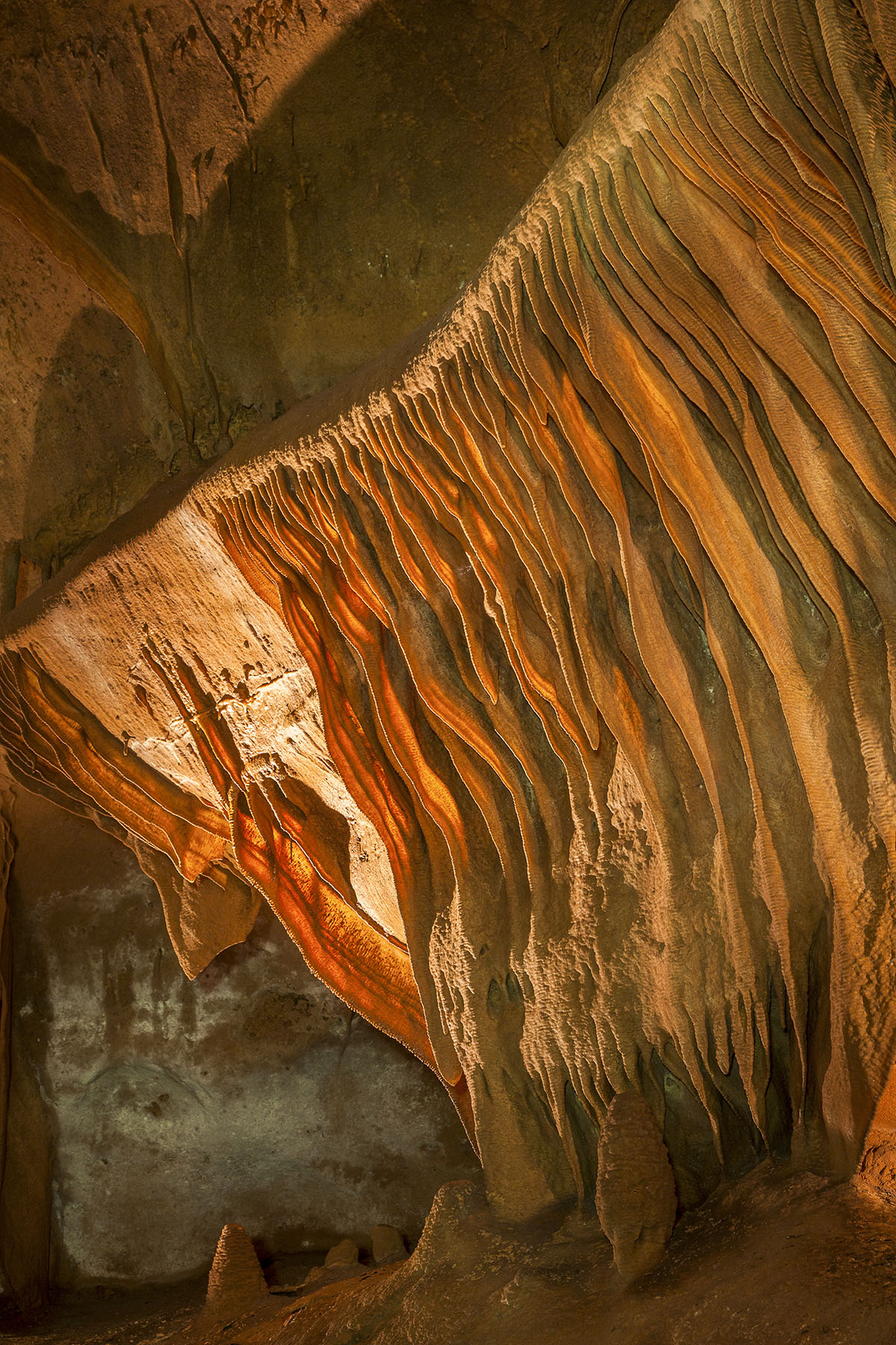 A photo of a bright, rust-orange cave with ribbon-like formations along the side