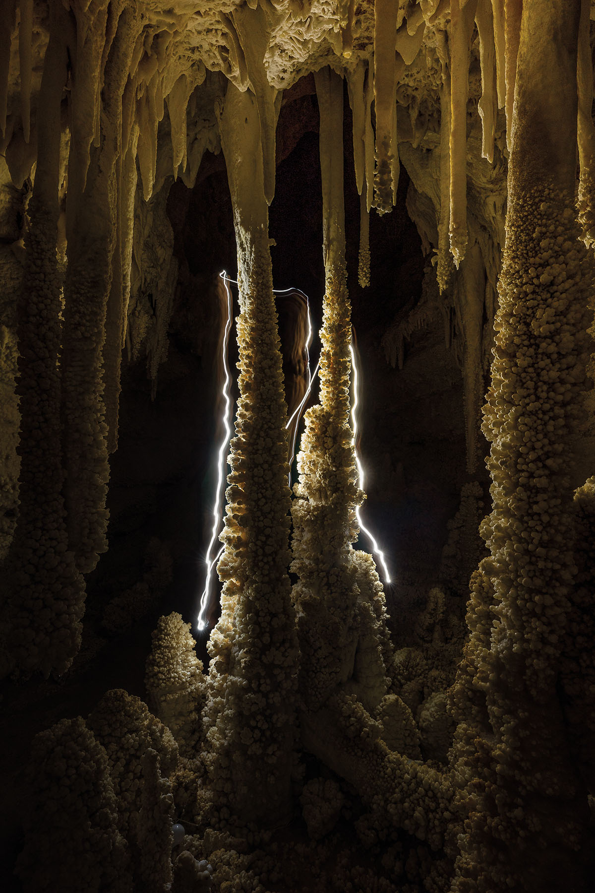 A photo of long exposure light trails around the formations inside of a dark cave in the Hall of White Giants room