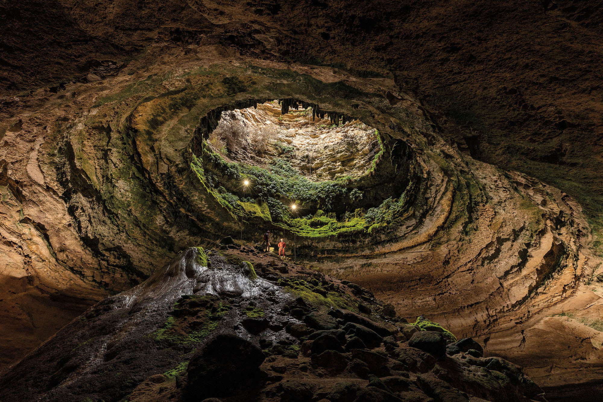 A view upward from inside a deep cave with moss and light