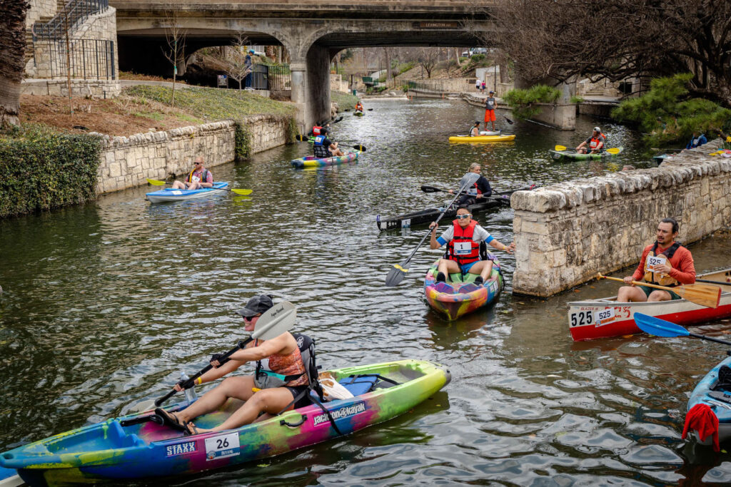 A photo of a group of people paddling kayaks and canoes along the San Antonio riverwalk