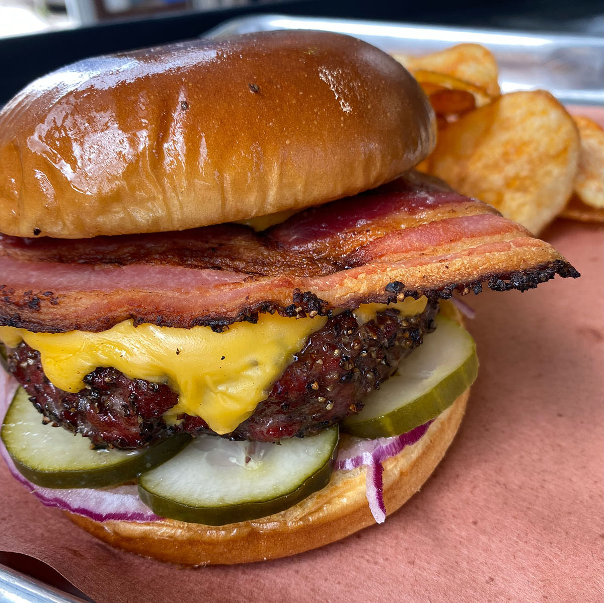 A burger piled high with green pickles, a slab of beef with cheese, a piece of bacon and a golden bun