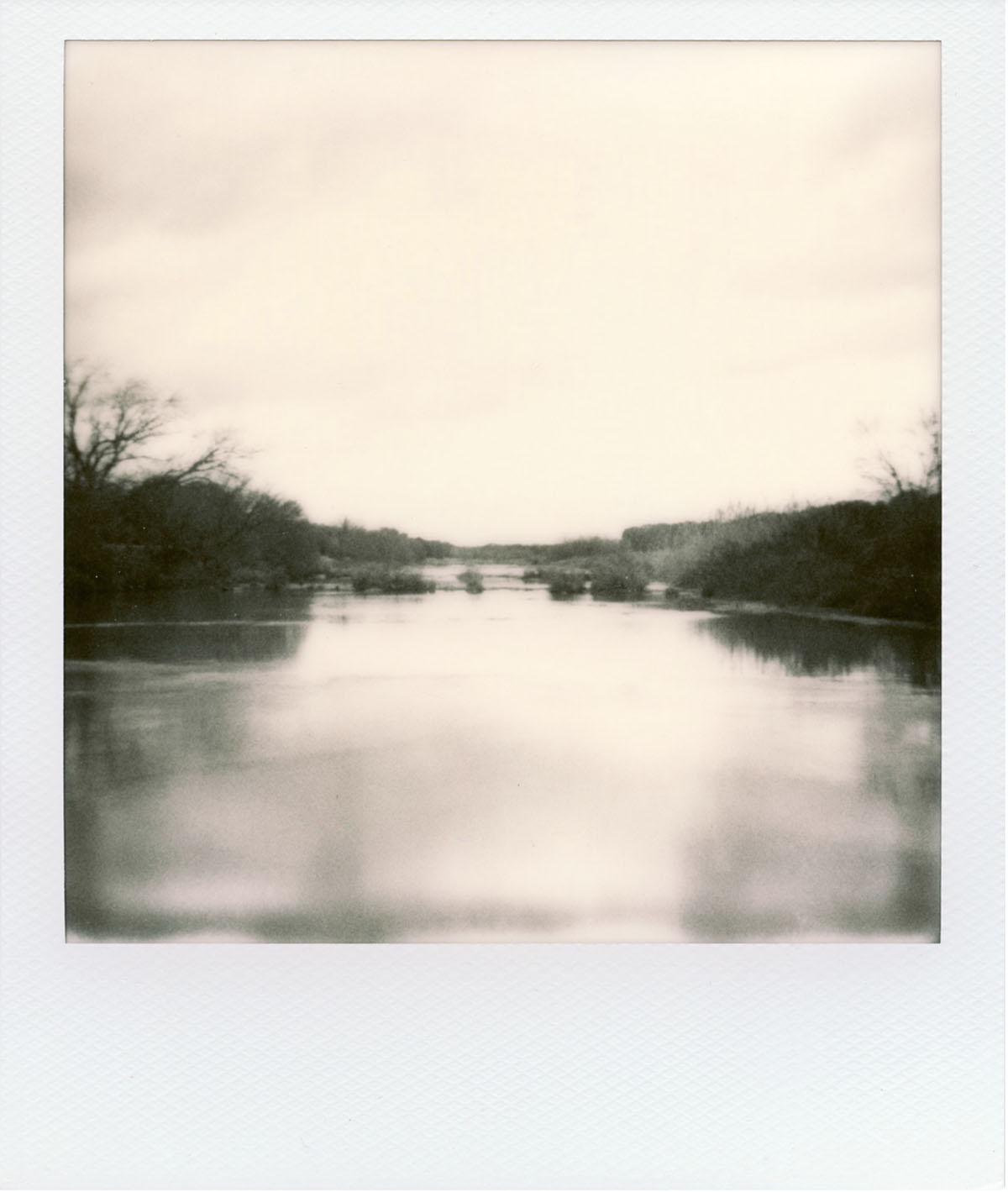 A Polaroid-style sepia tone picture of a body of water flanked by two grassy banks under a yellow-tone sky