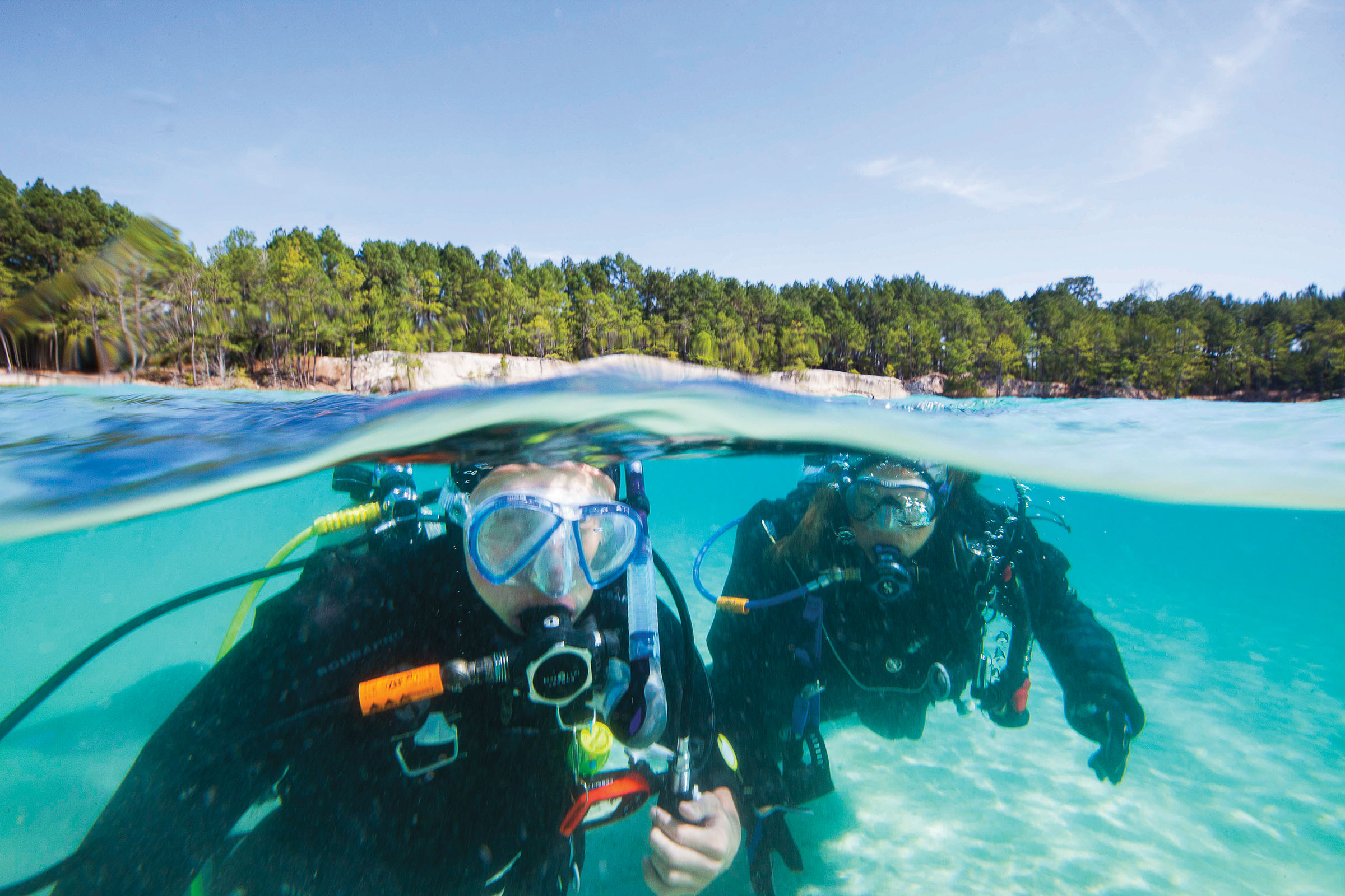 A picture of two people in scuba diving equipment in bright blue water under blue sky