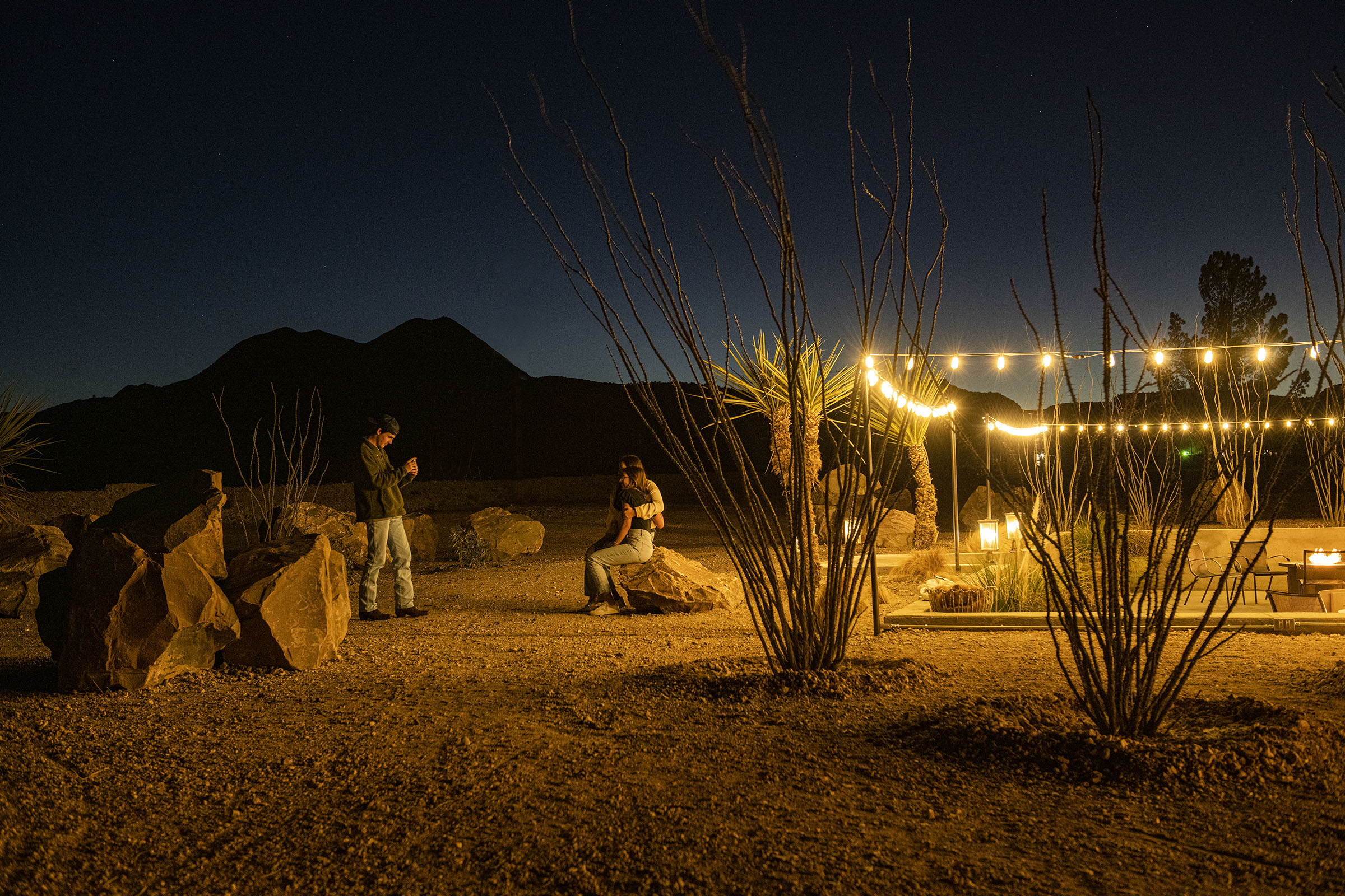 An image of people sitting on rocks in soft light under a dark star-filled sky