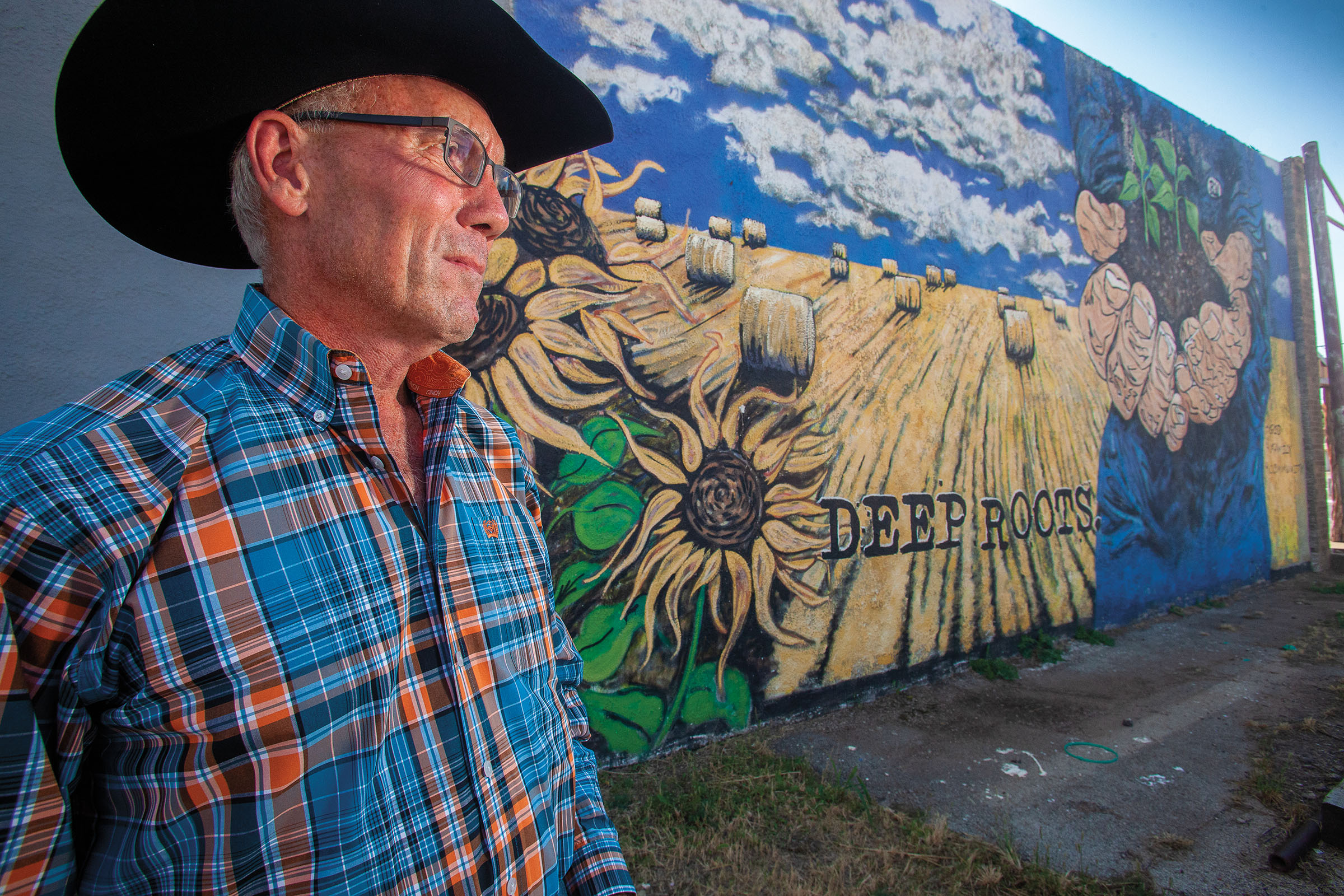 A picture of a man in a black cowboy hat standing in front of a mural of painted sunflowers