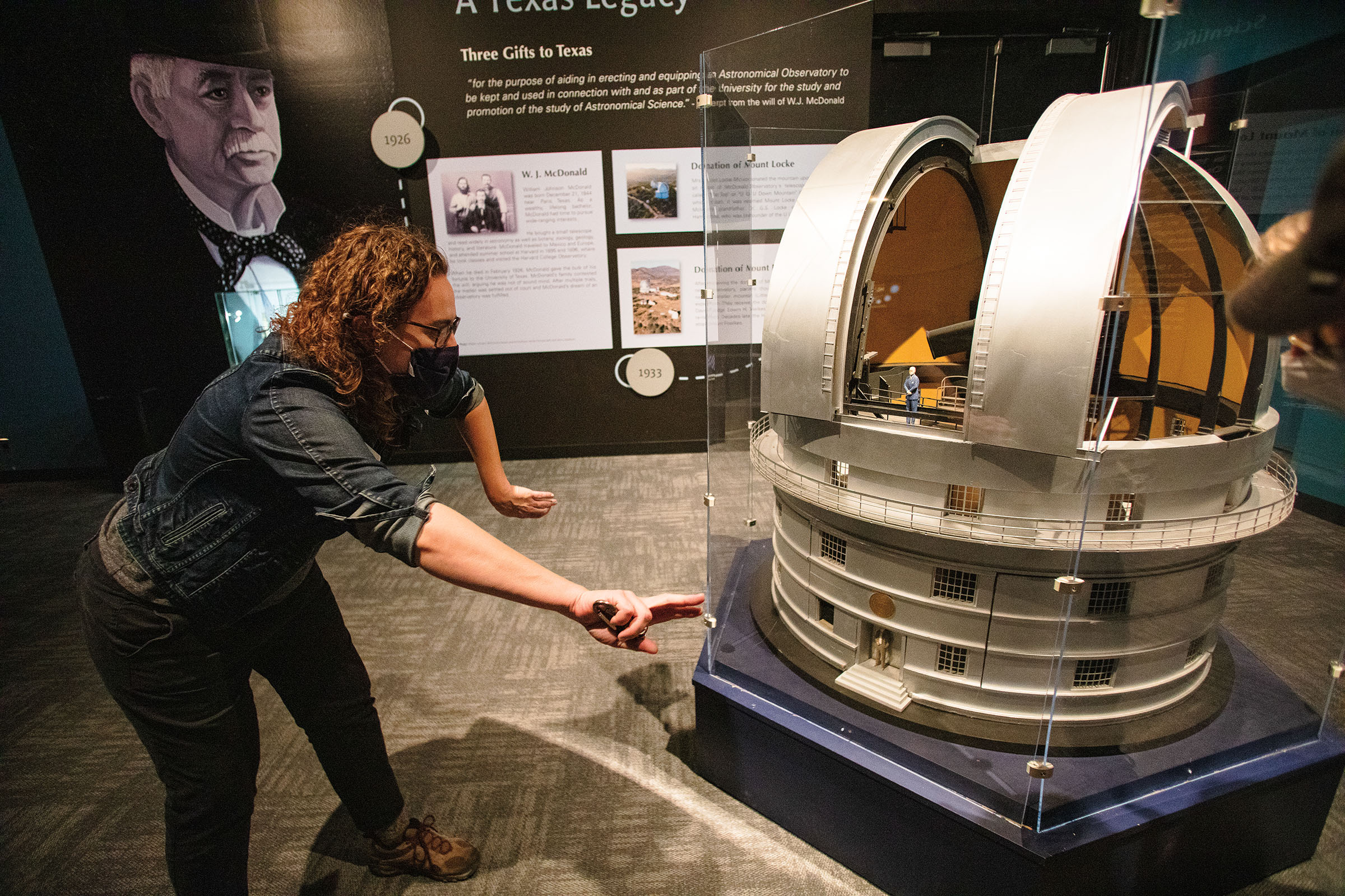 A picture of a person leaning over and pointing out features on a small-scale model of a white telescope