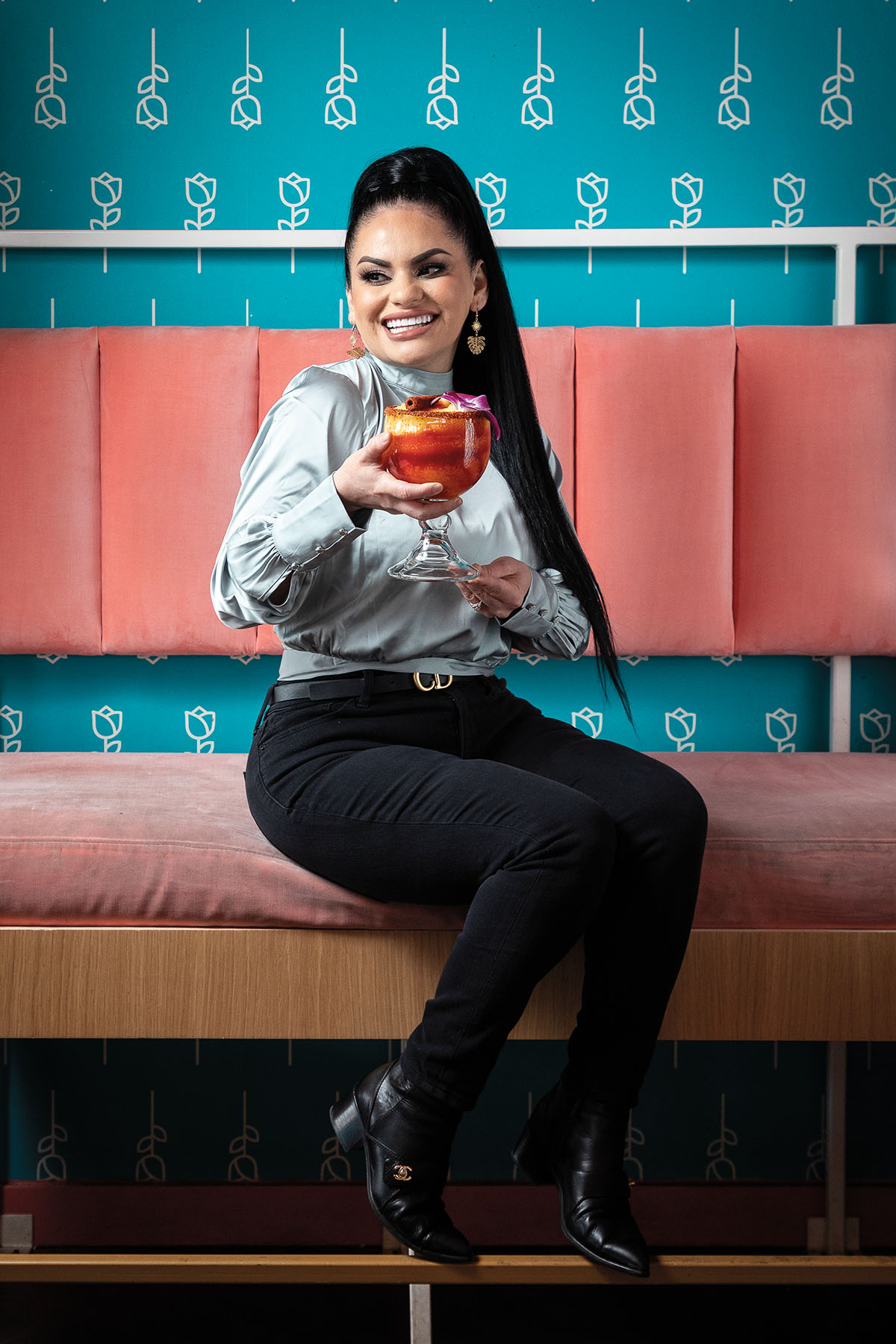 A picture of a woman with long black hair sits on a bright pink booth holding a large frozen drink