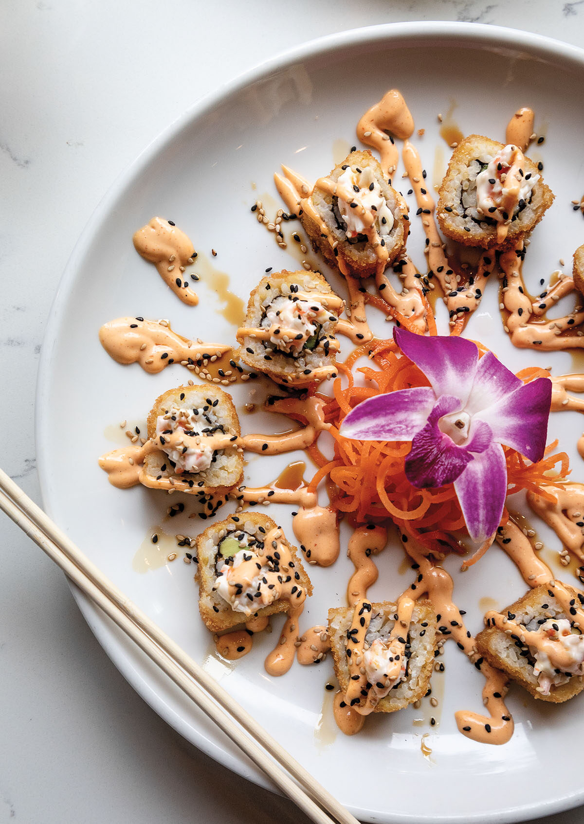 A picture of sushi with a pink/orange sauce on a white plate with a bold purple flower in the center